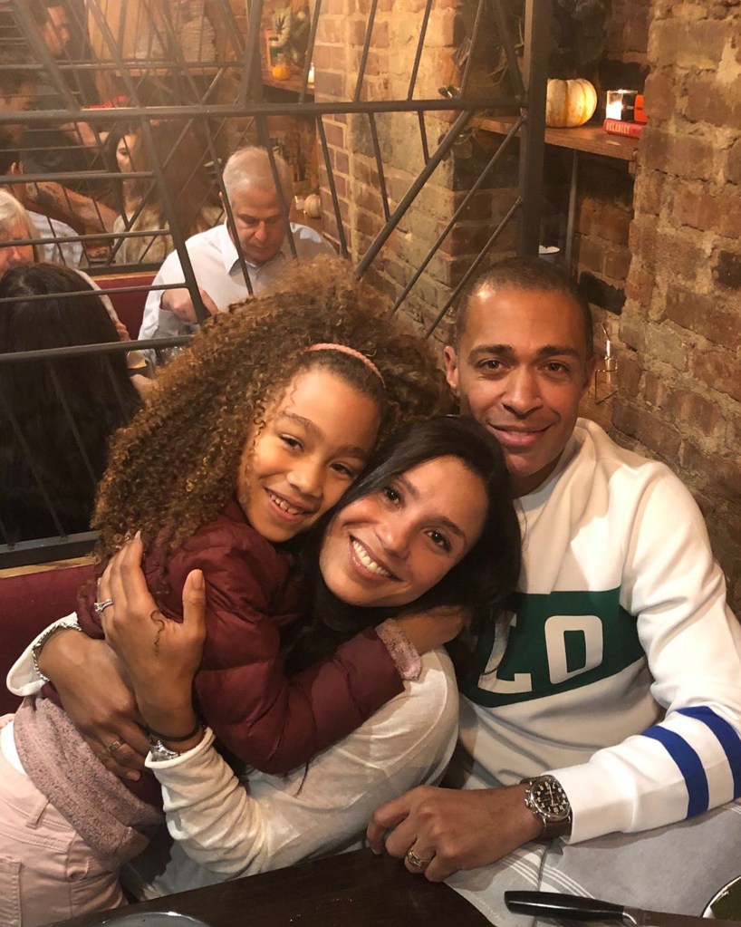 A family of three, a child with curly hair and two adults, smiling at the camera in a restaurant.