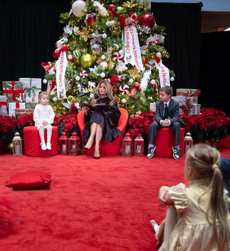 First Lady Melania Trump reading to young children by Christmas tree.