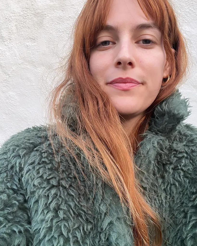 Riley Keough with red hair wearing a green fur coat.