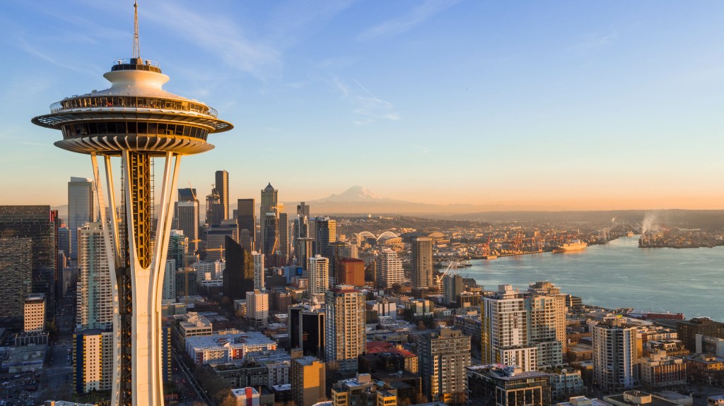Aerial view of the Seattle skyline at sunset, with the Space Needle in the foreground and Mount Rainier in the background.