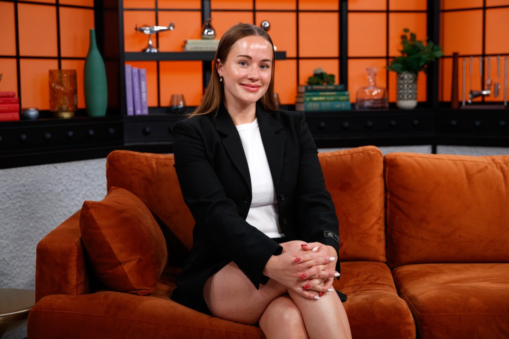 Whitney Leavitt smiling while seated on an orange couch.