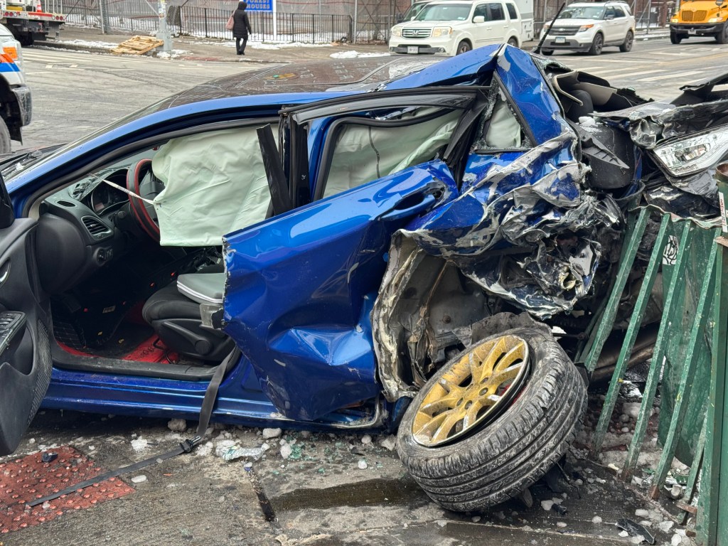 A blue car heavily damaged from a crash, with the side of the car ripped open and an airbag deployed.