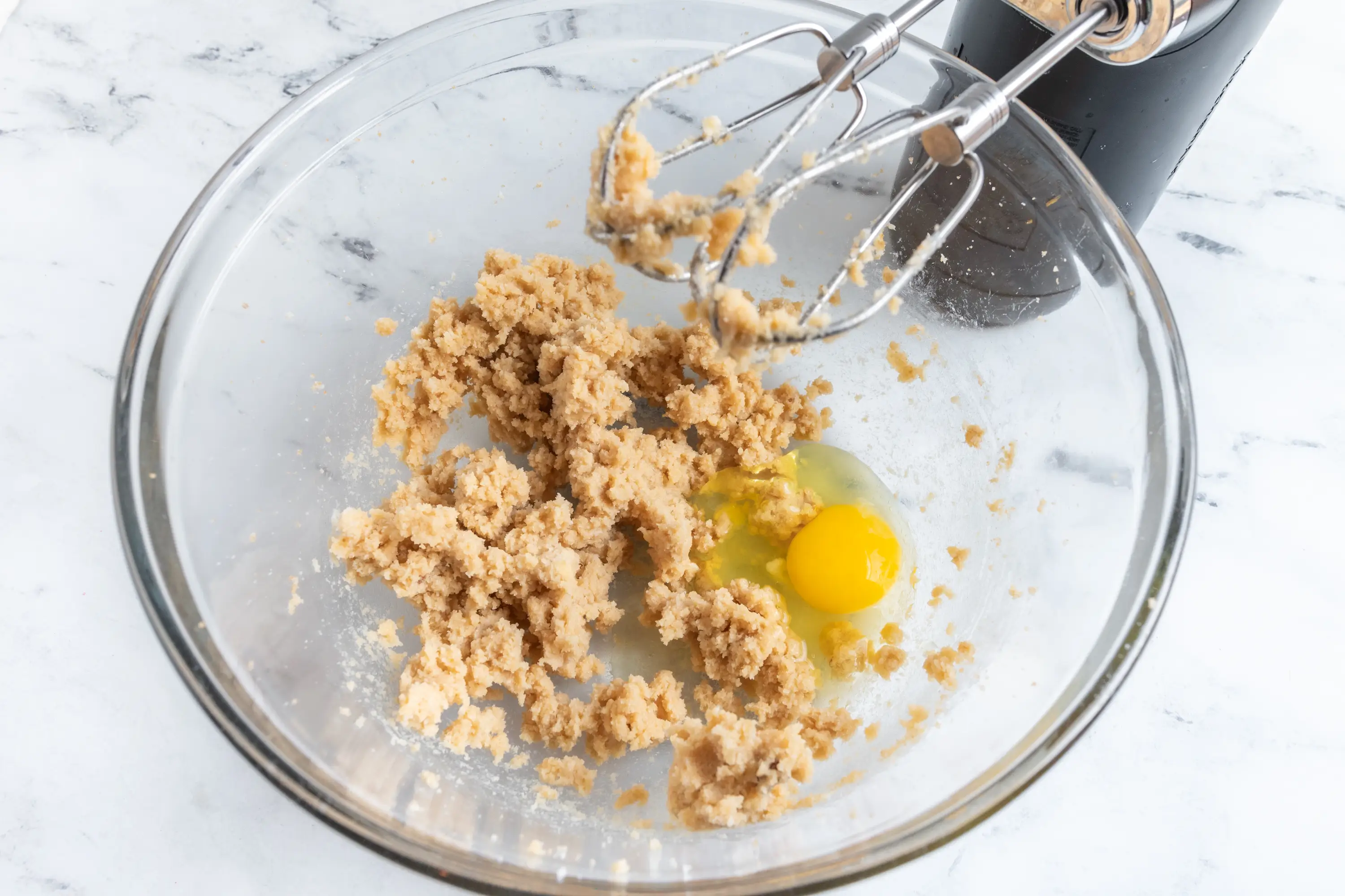 Egg, and sugars creamed with butter in glass bowl with hand mixer attachments above it