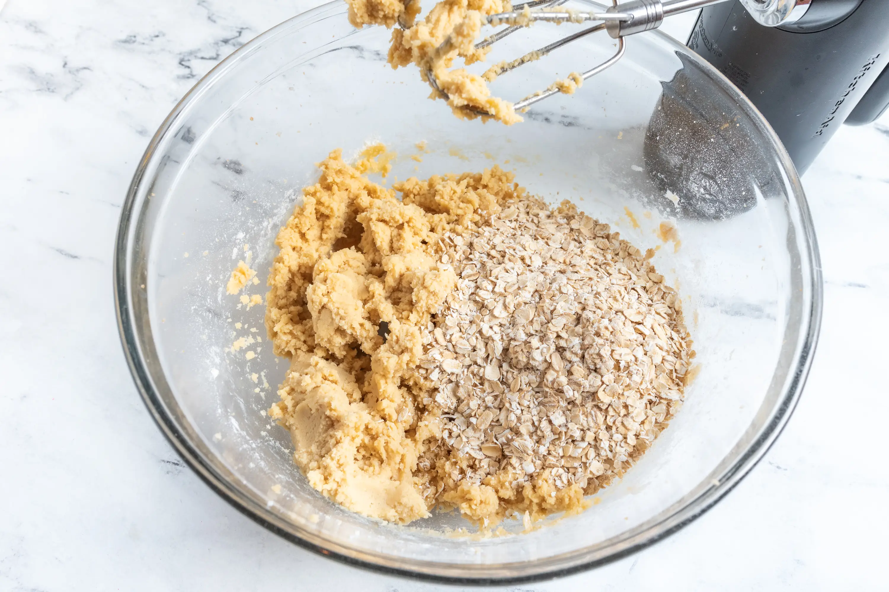 Oats on top of creamed butter and sugar mixture in glass bowl