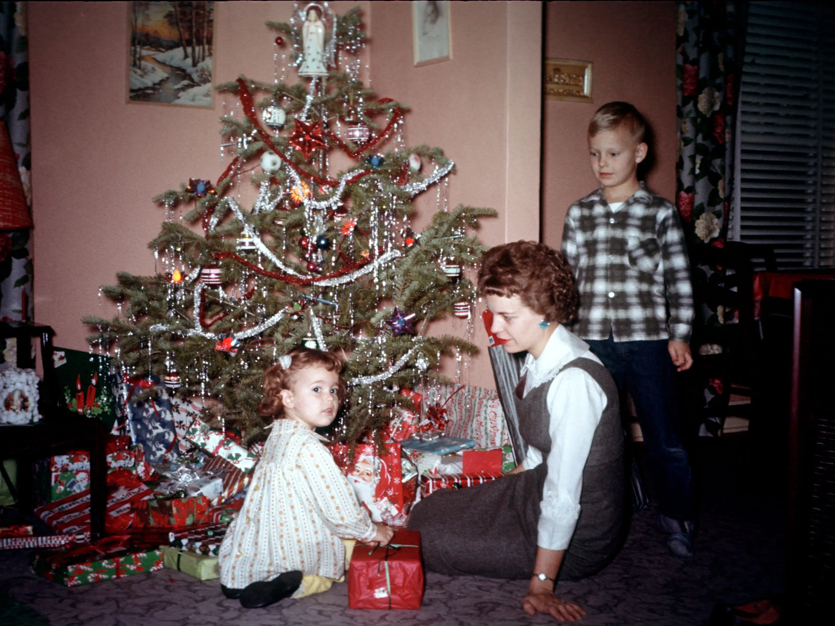 A family gathers around the Christmas tree while a young girl opens her present.