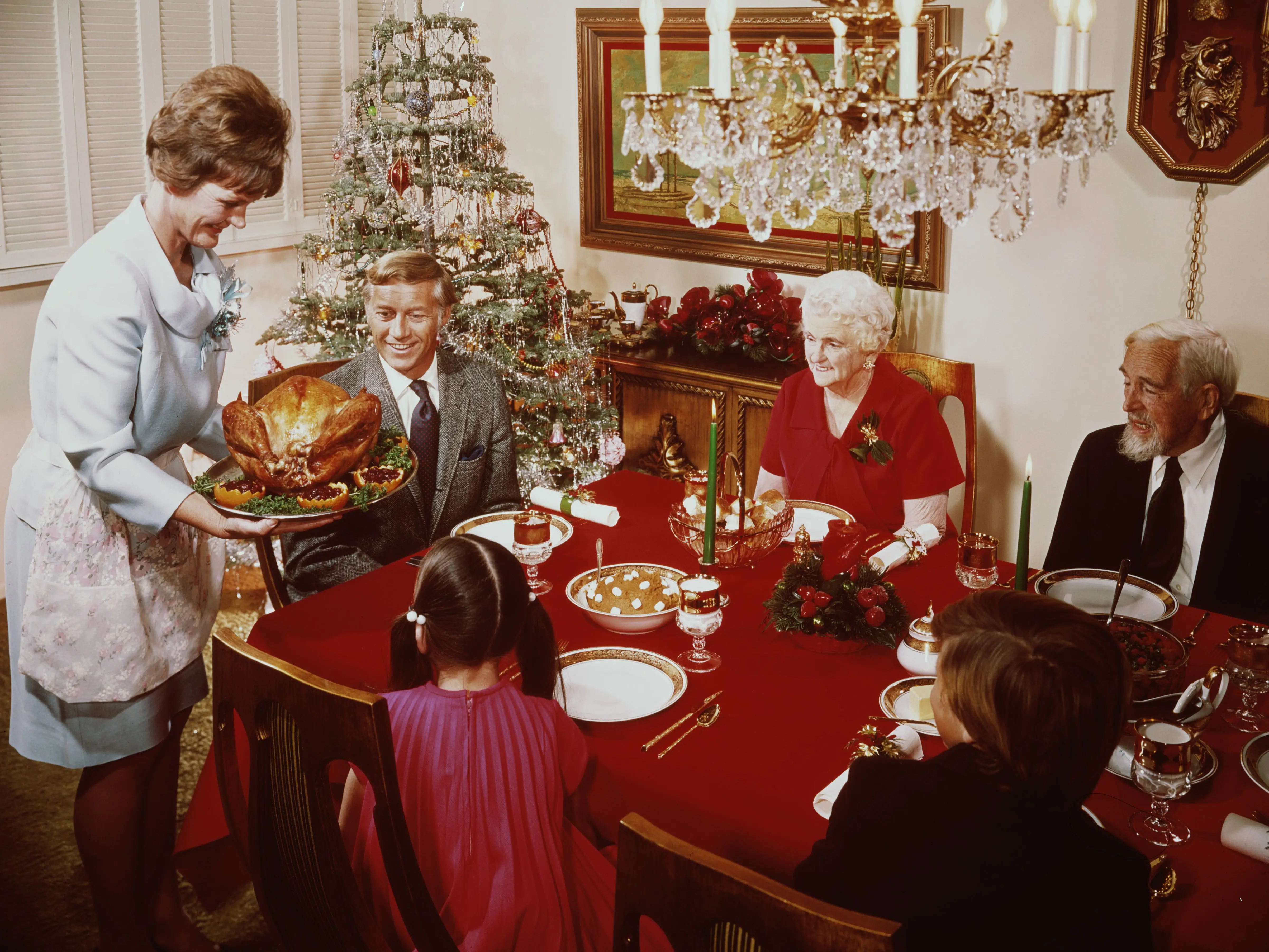 A mother bringing a large turkey to the table for Christmas dinner, circa 1965.