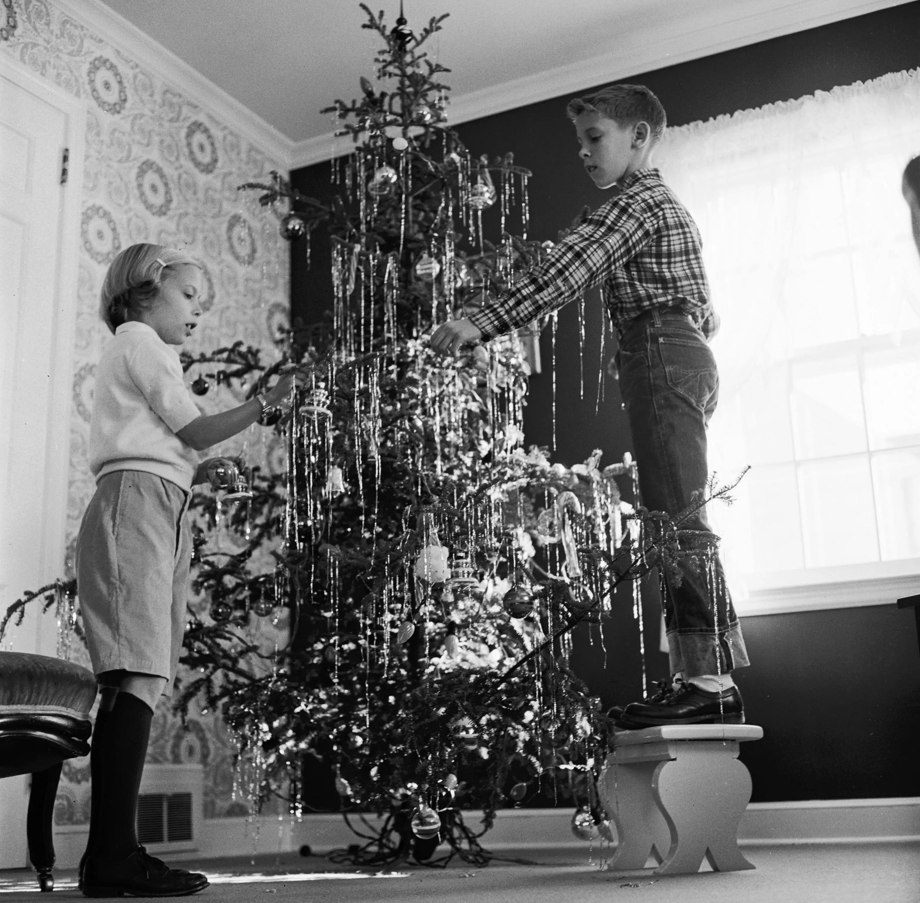 A boy and his sister decorate a Christmas tree with tinsel in 1955