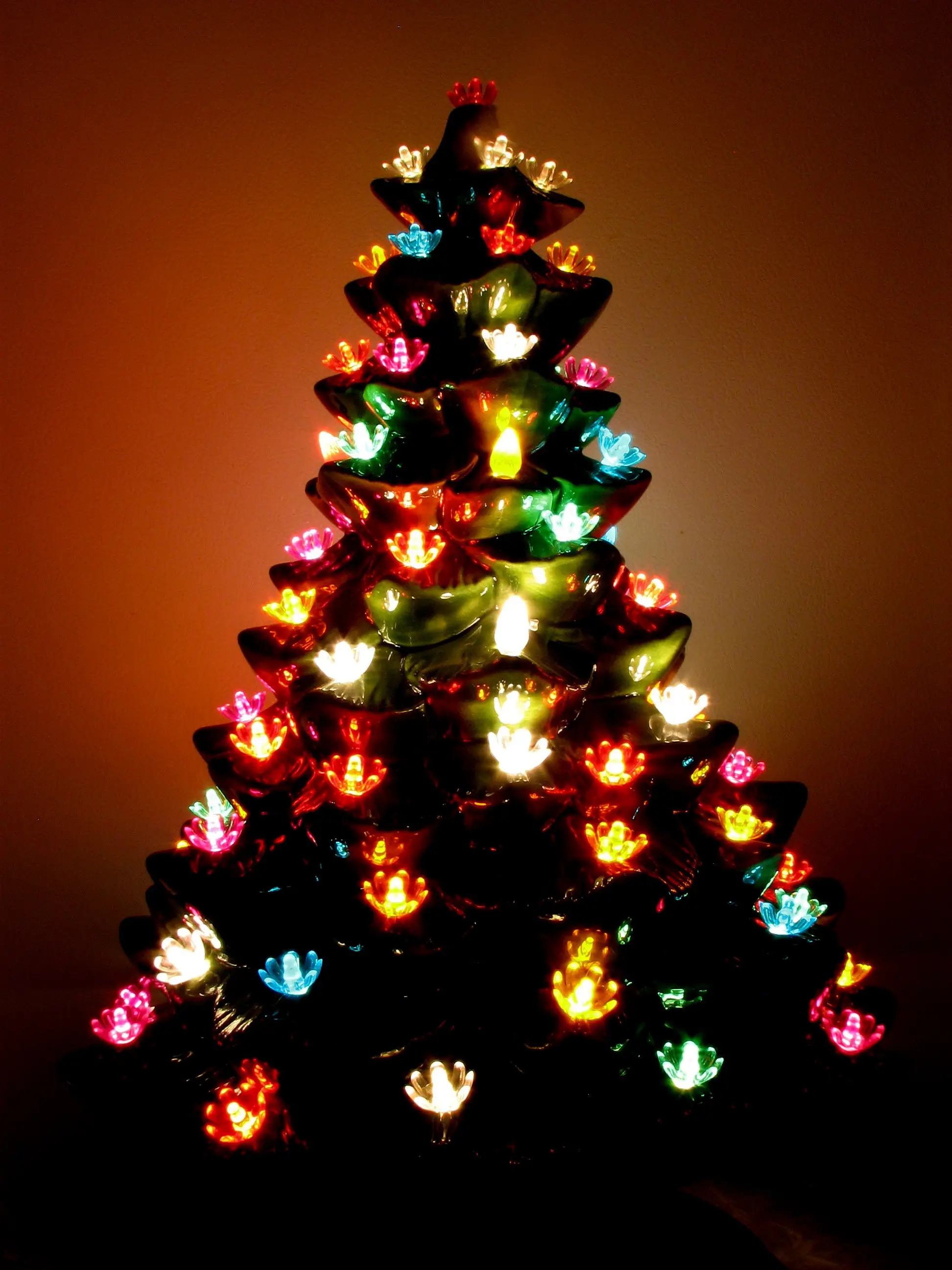 Vintage tabletop glazed ceramic bisque Christmas tree with multicolored lights in dark.