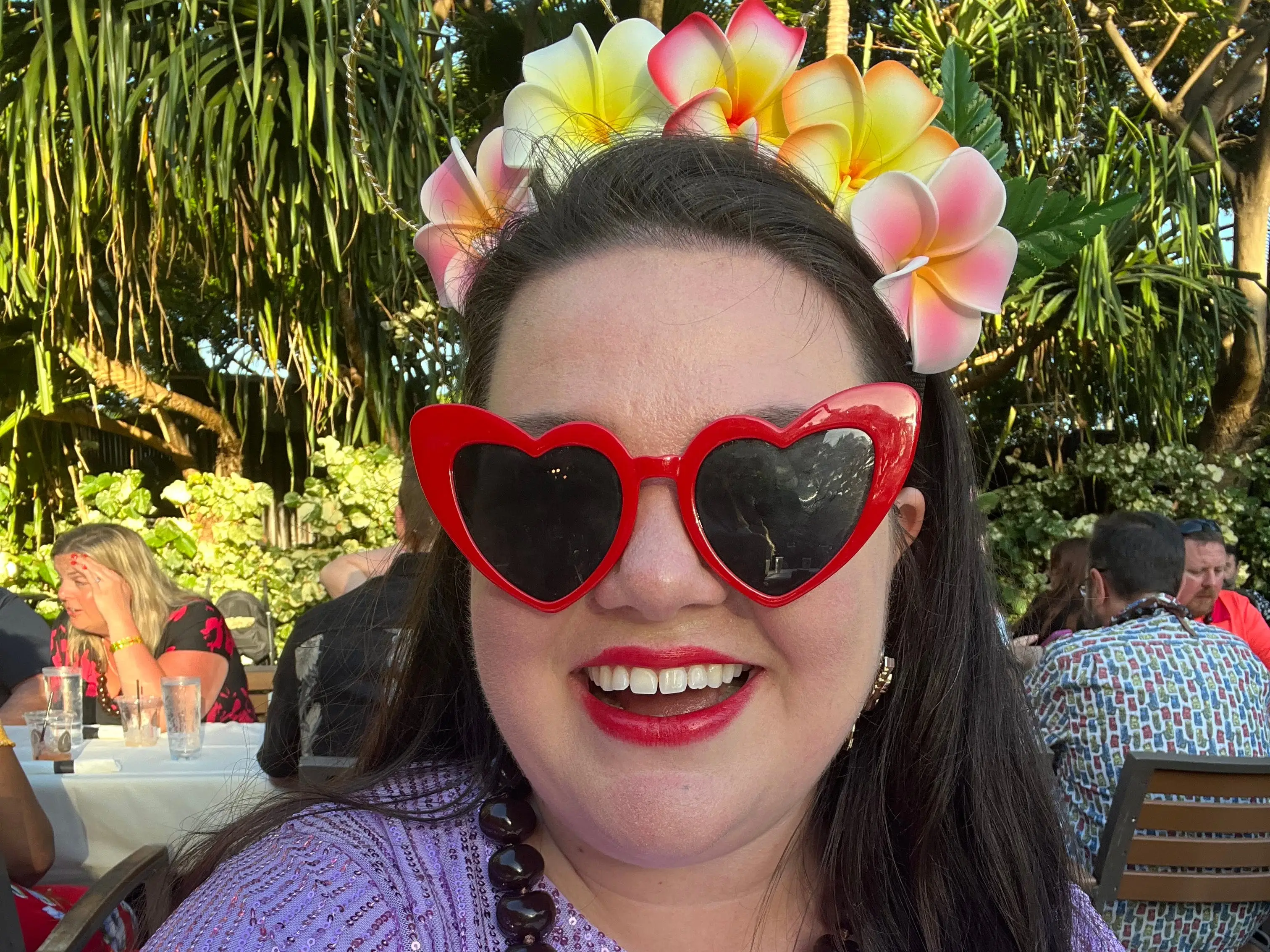 The author wearing red heart-shaped sunglasses, a lei crown, and a beaded necklace.