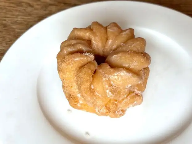 A cruller doughnut topped with a glaze on a white plate