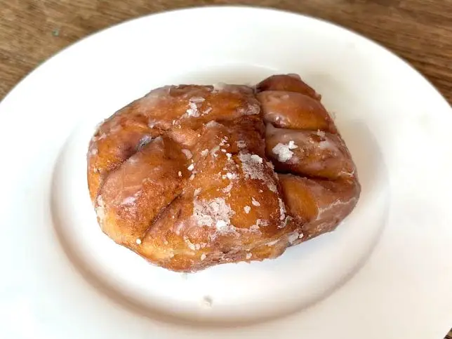 A fritter-like doughnut topped with a glaze on a white plate.