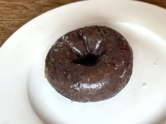 A chocolate cake doughnut topped with a glaze on a white plate.