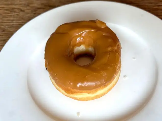 A doughnut topped with a light-brown icing on a white plate.