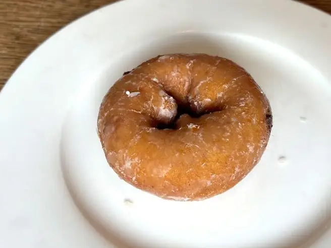 A cake doughnut topped with a glaze on a white plate.