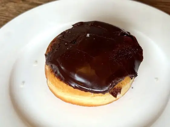 A Boston cream doughnut topped with chocolate icing on a white plate.