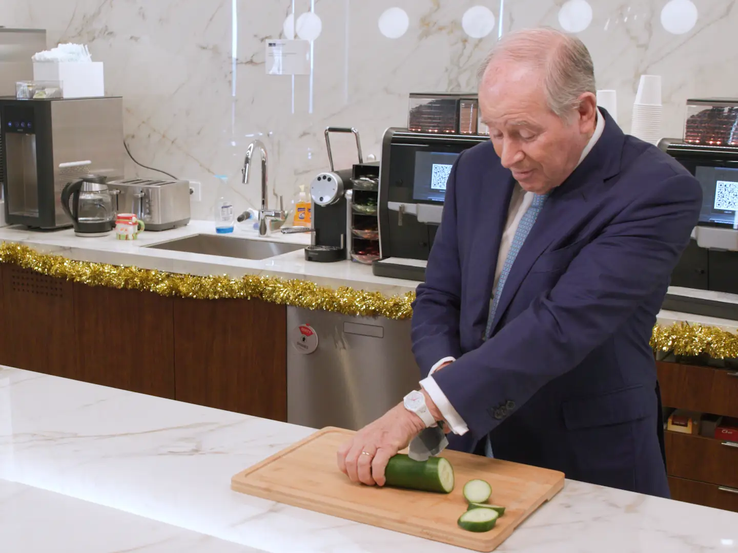 Steve Schwarzman cutting a cucumber awkwardly on a granite countertop in an office kitchen.