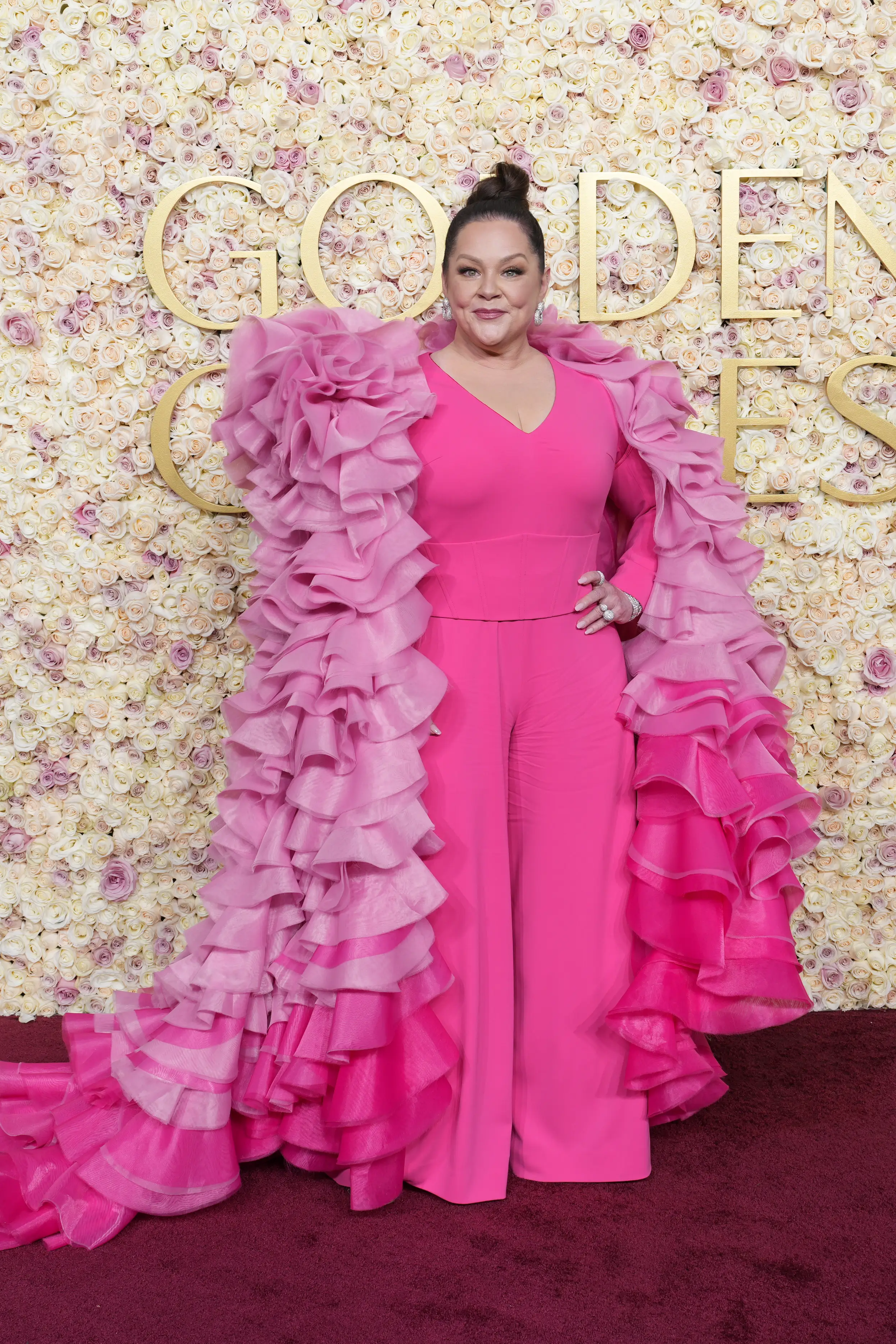 Melissa McCarthy on the Golden Globes red carpet wearing a pink jumpsuit with a pink frilly cloak.