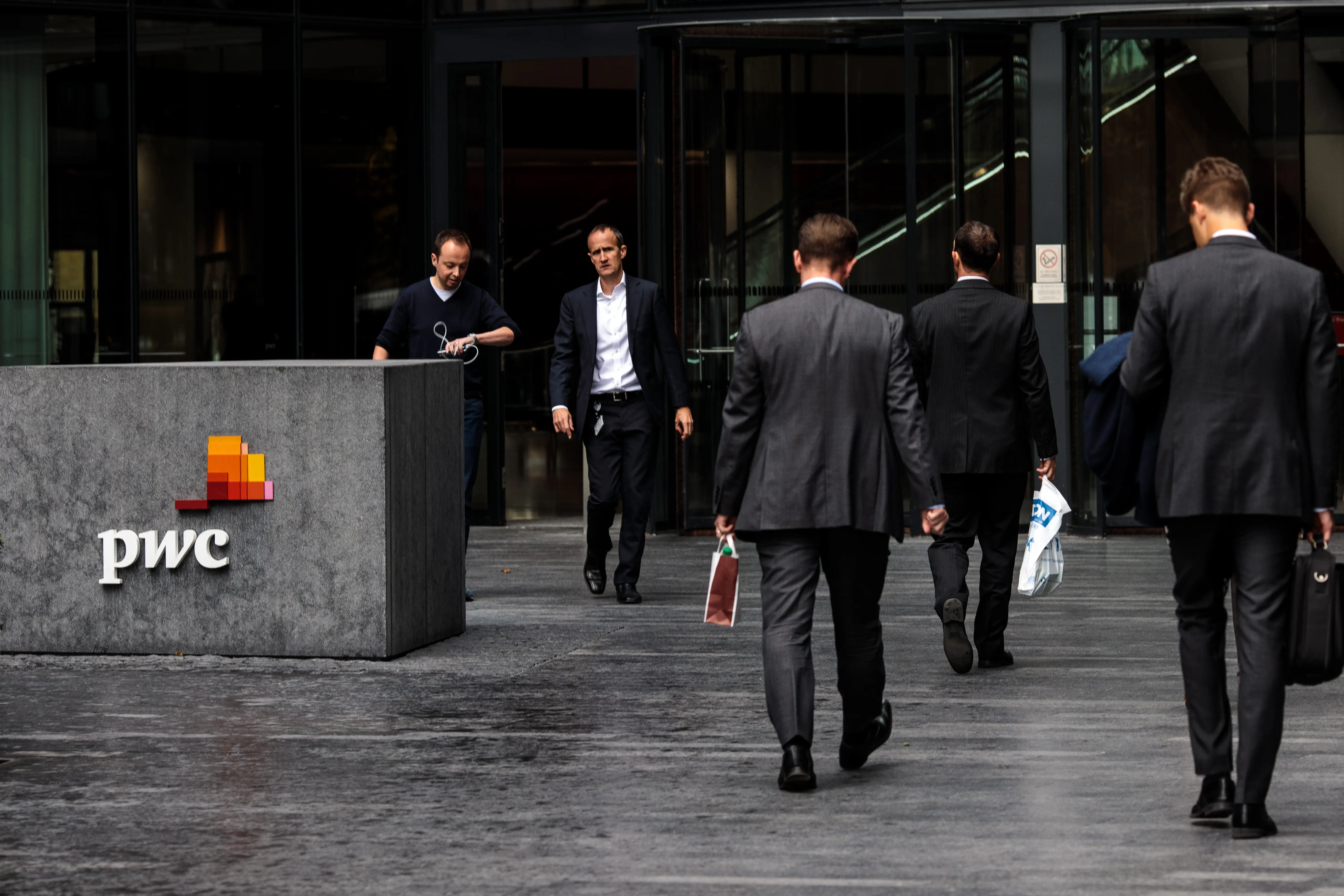 Men in suits next to a PwC logo outside a grey glass building