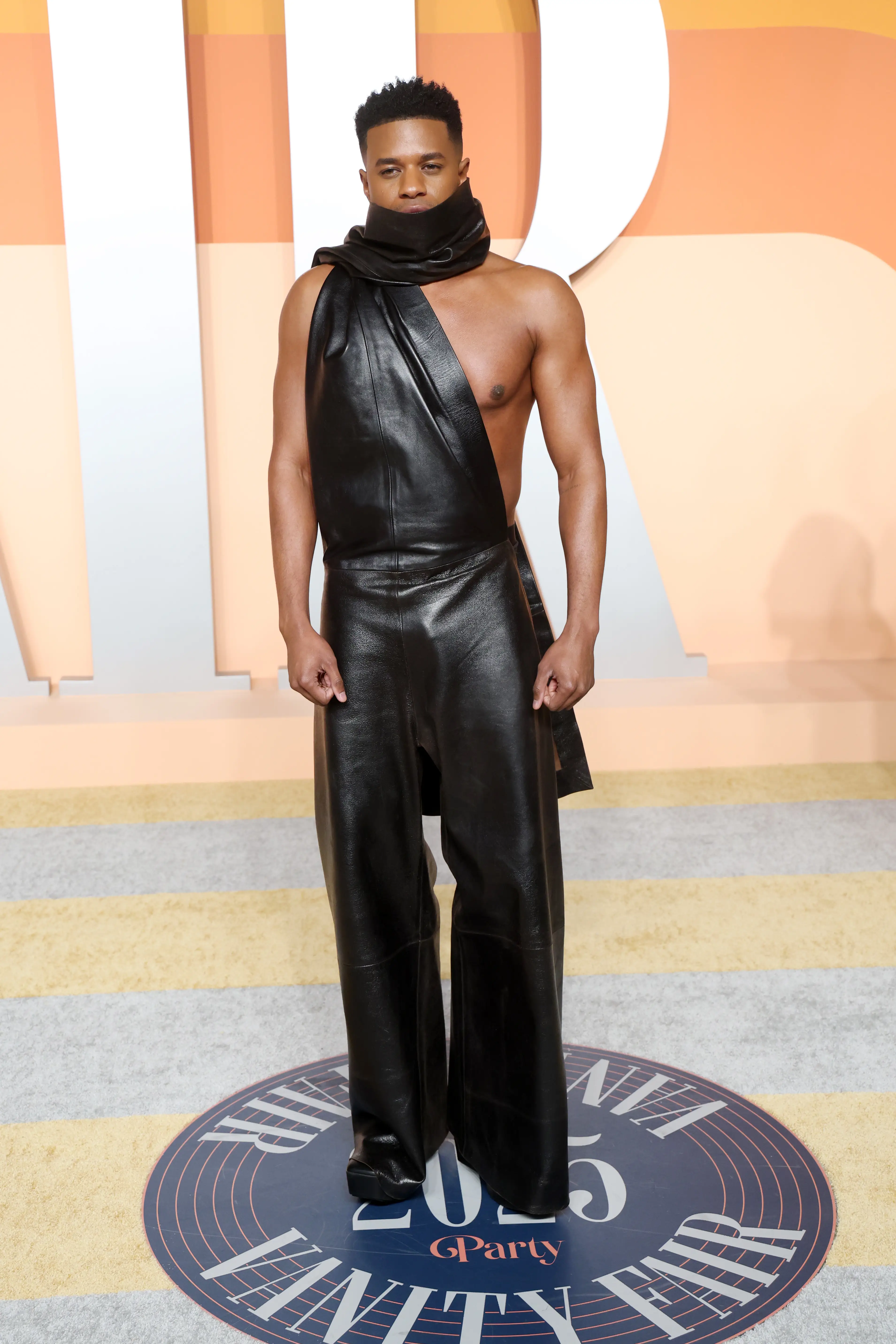Jeremy Pope wearing a leather jumpsuit with a thick neckscarf Vanity Fair Oscar party.