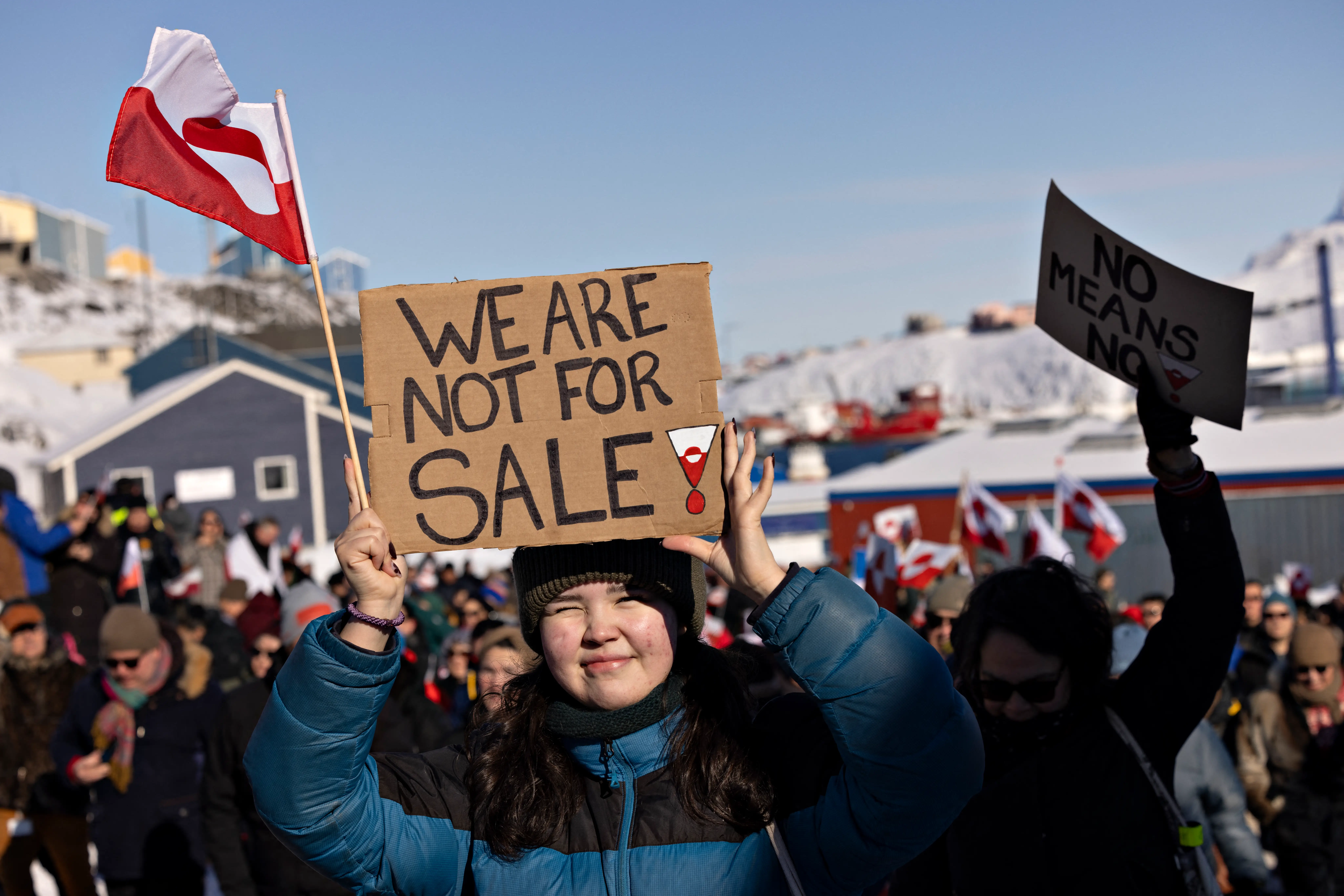 A person in a blue and black jacket holds a cardboard sign that says we are not for sale