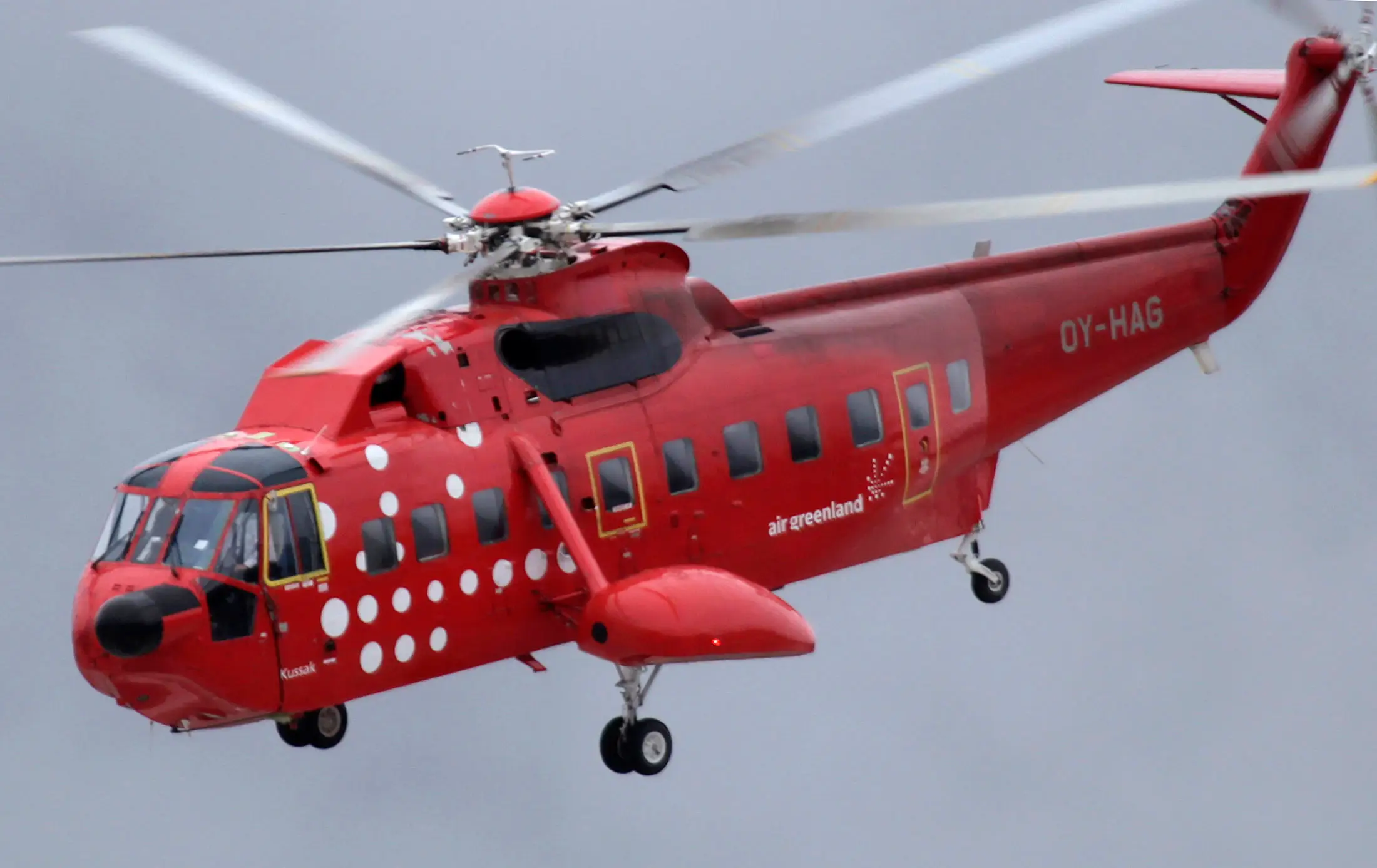 A red helicopter flies with air Greenland written on its side