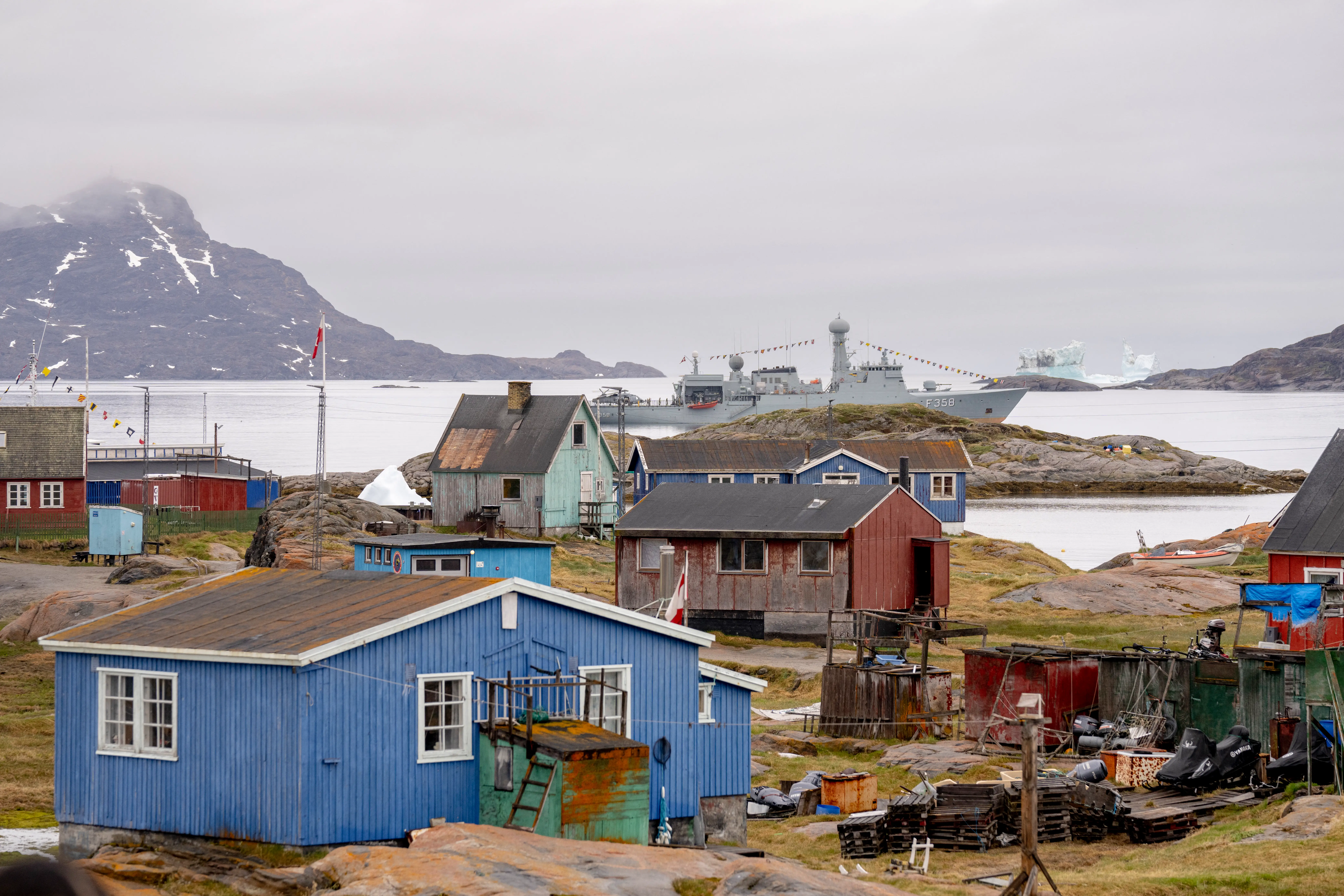 Small colorful houses with water, a ship, and dirt-covered hills in the background