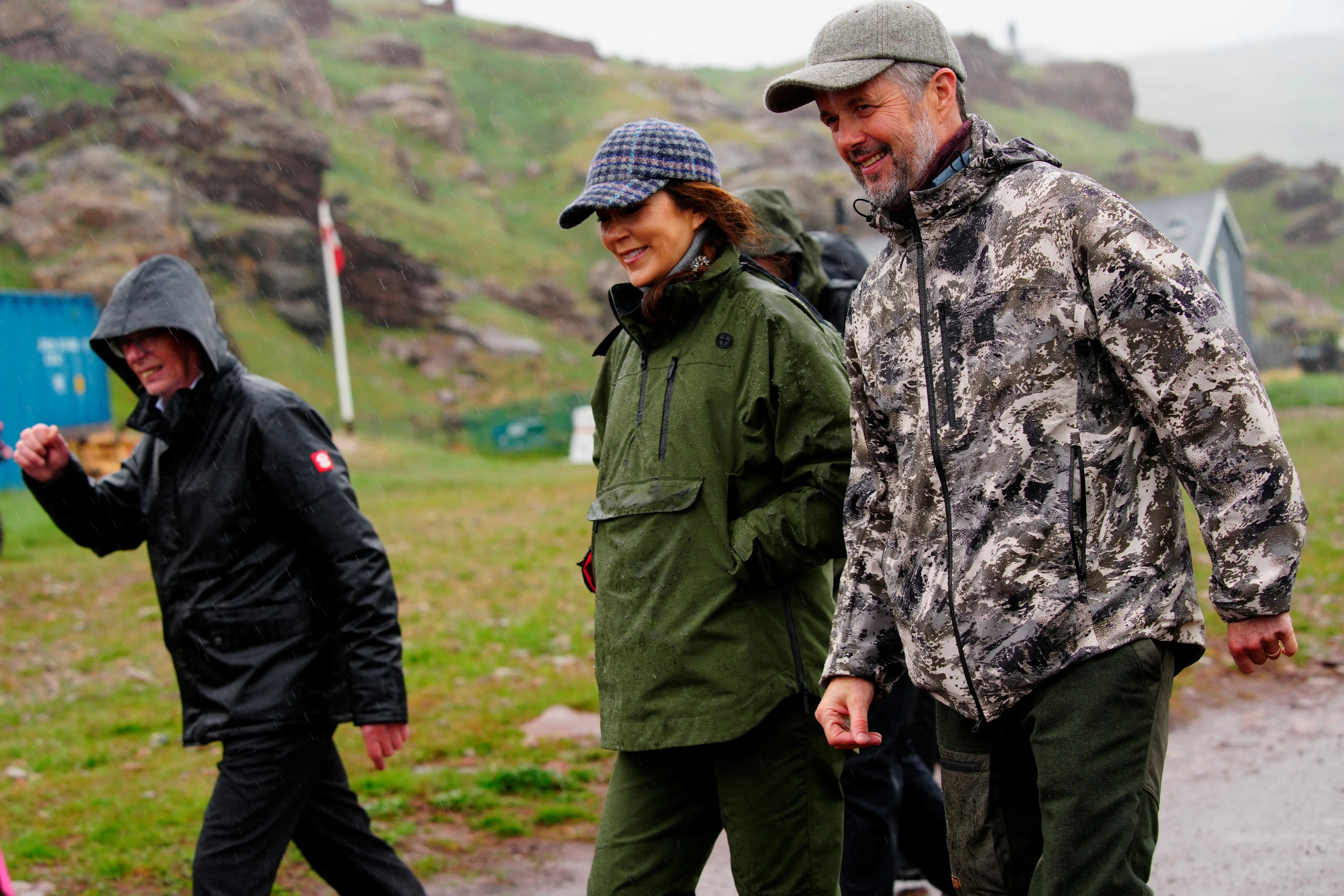 Denmark's King Frederik and Queen Mary wear spring jackets and baseball hats with green hills in the background