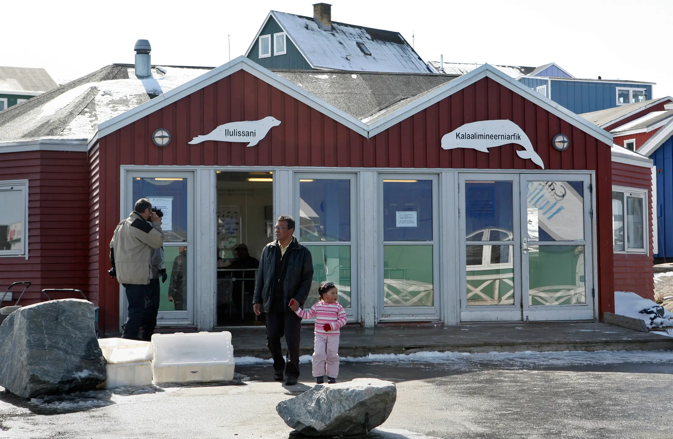 People walk out of a red building with white signs in the shape of a seal and whale on it