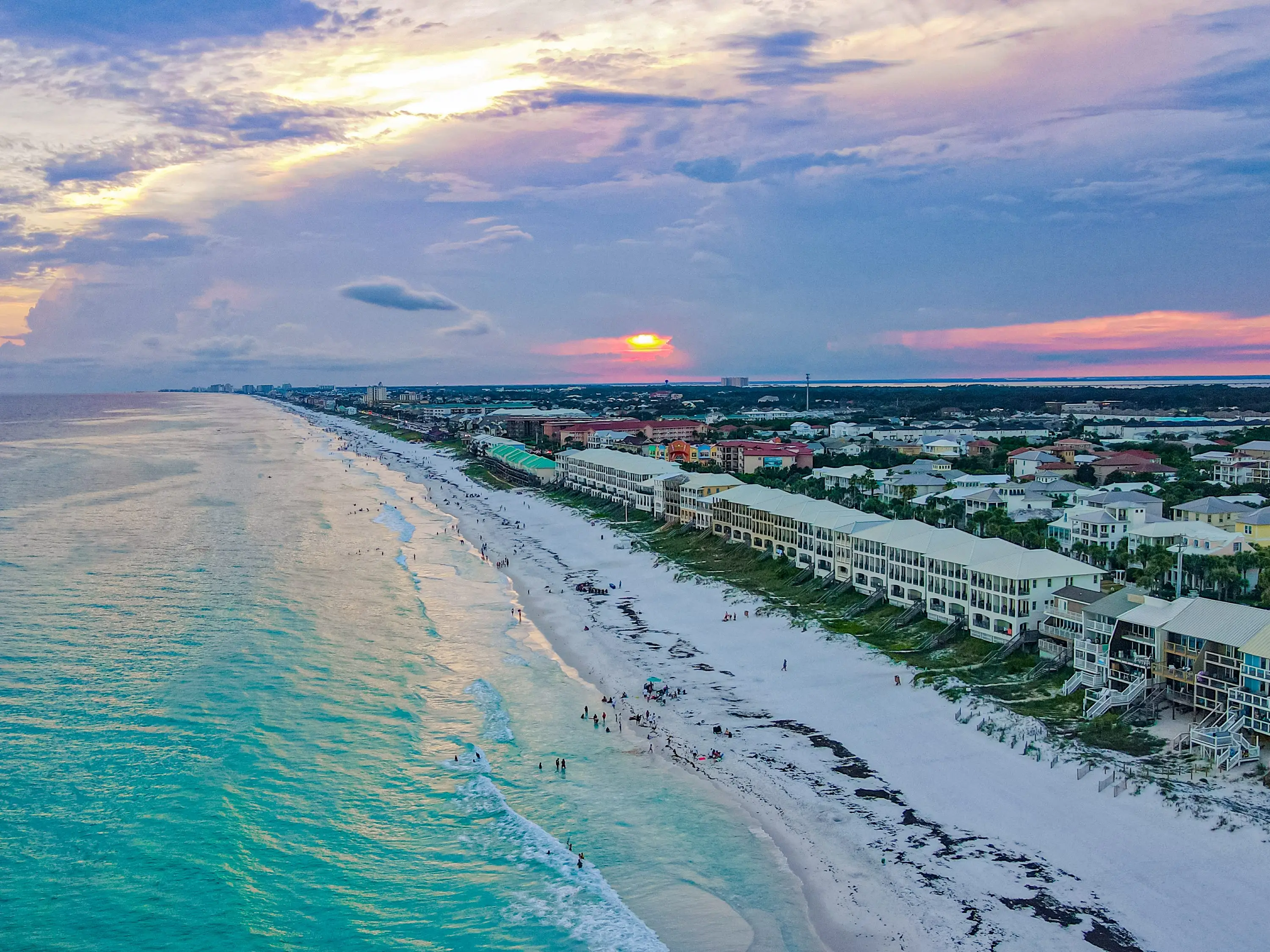 An aerial view of a beach at sunset, with houses along the dunes.