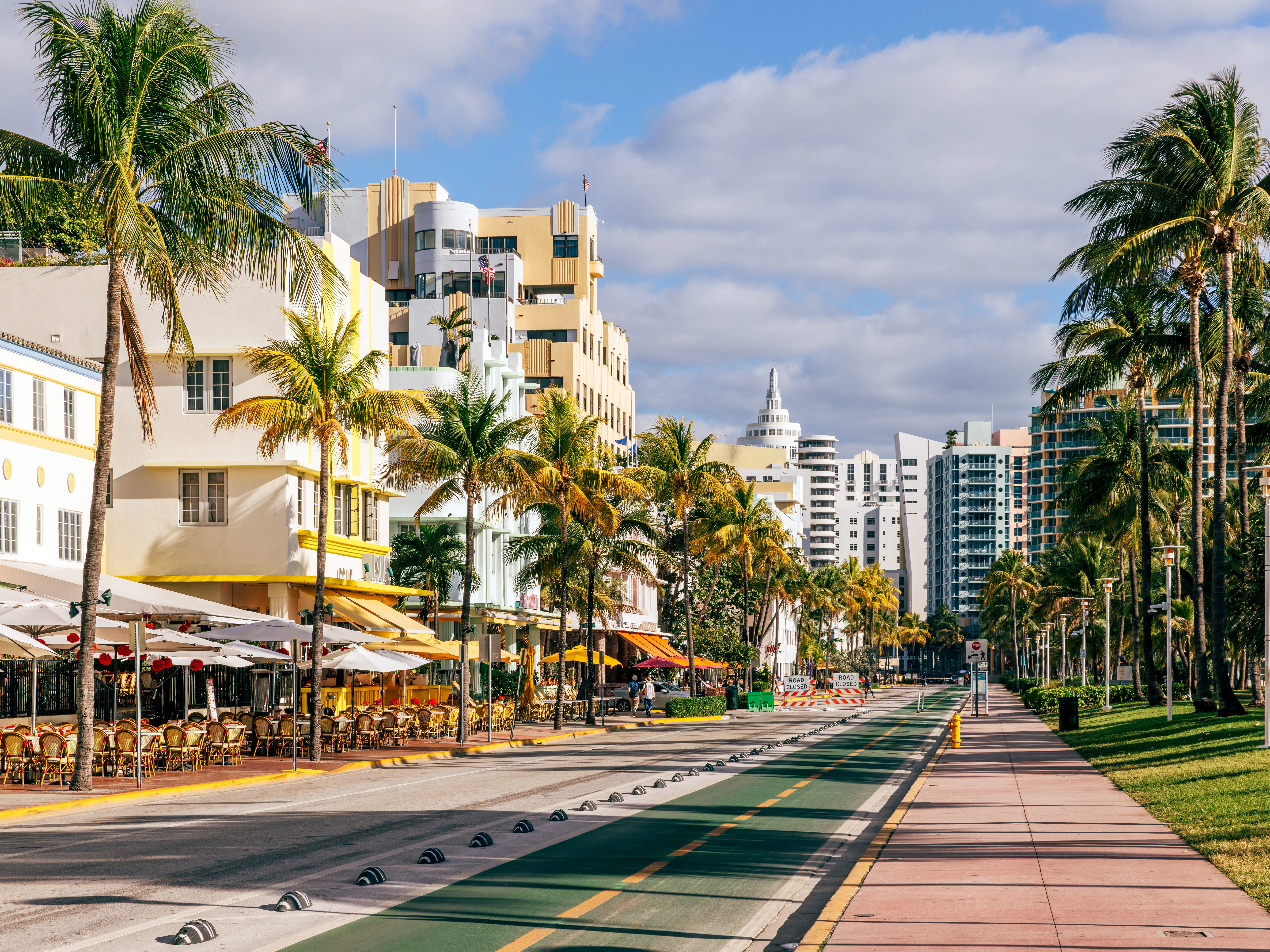 A street lined with Art Deco buildings, restaurants, and palm trees in Miami.