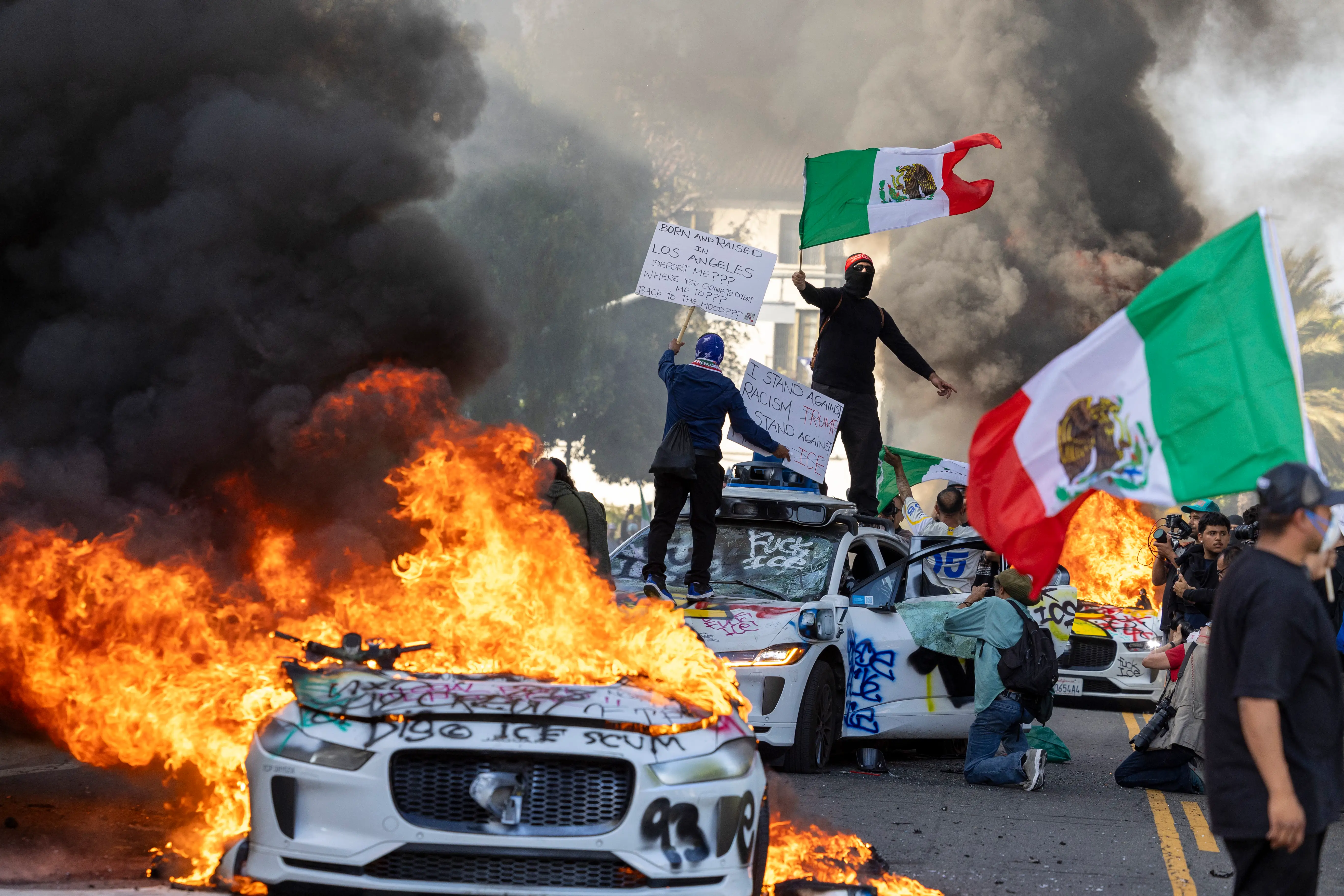 Protestors standing on Waymo vehicles with flags in Los Angeles protests