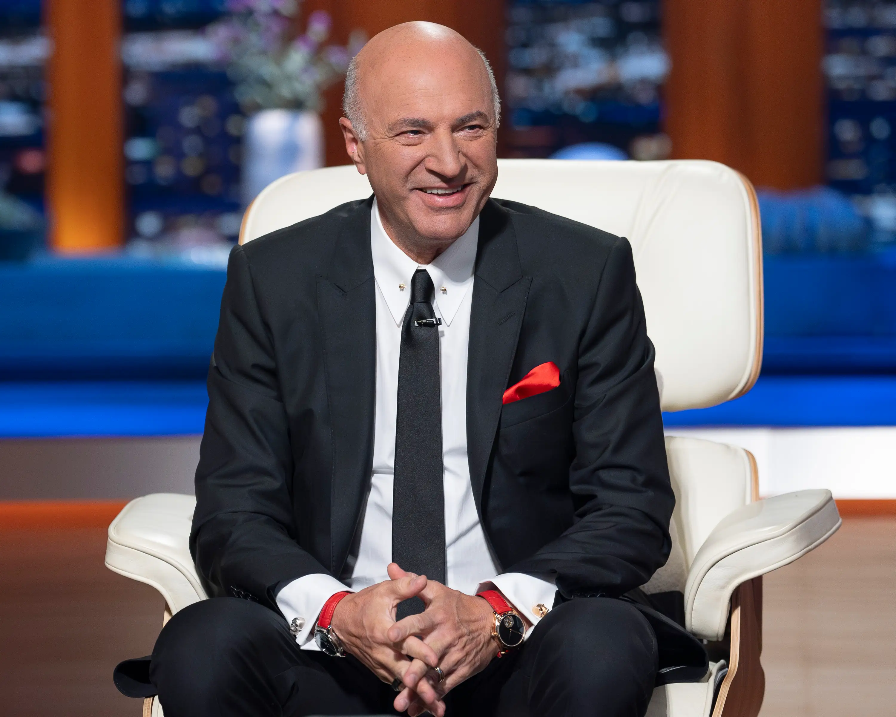 Kevin O'Leary wearing a suit and sitting on a white chair.