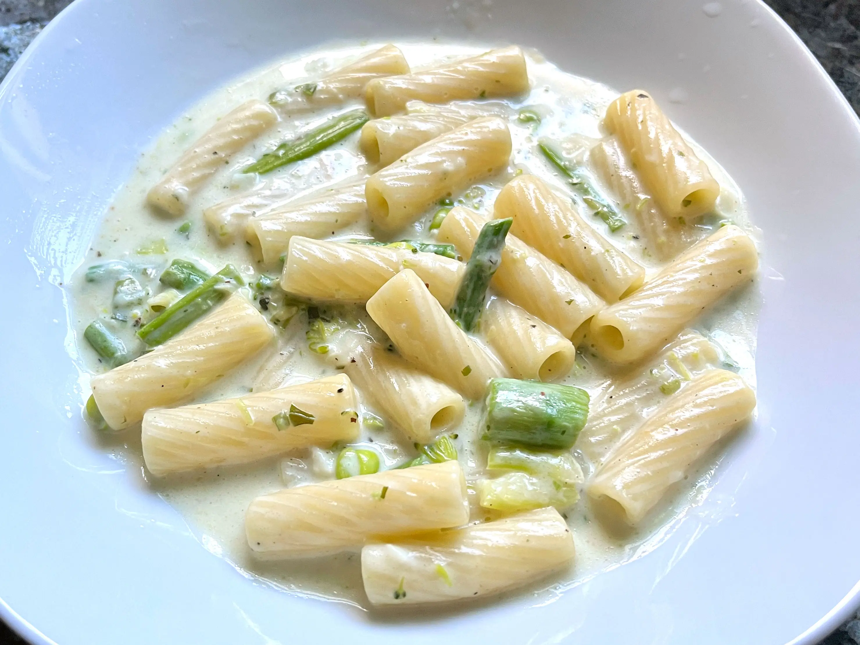 A plate of rigatoni with asparagus, broccoli, and green peas in a cream sauce.