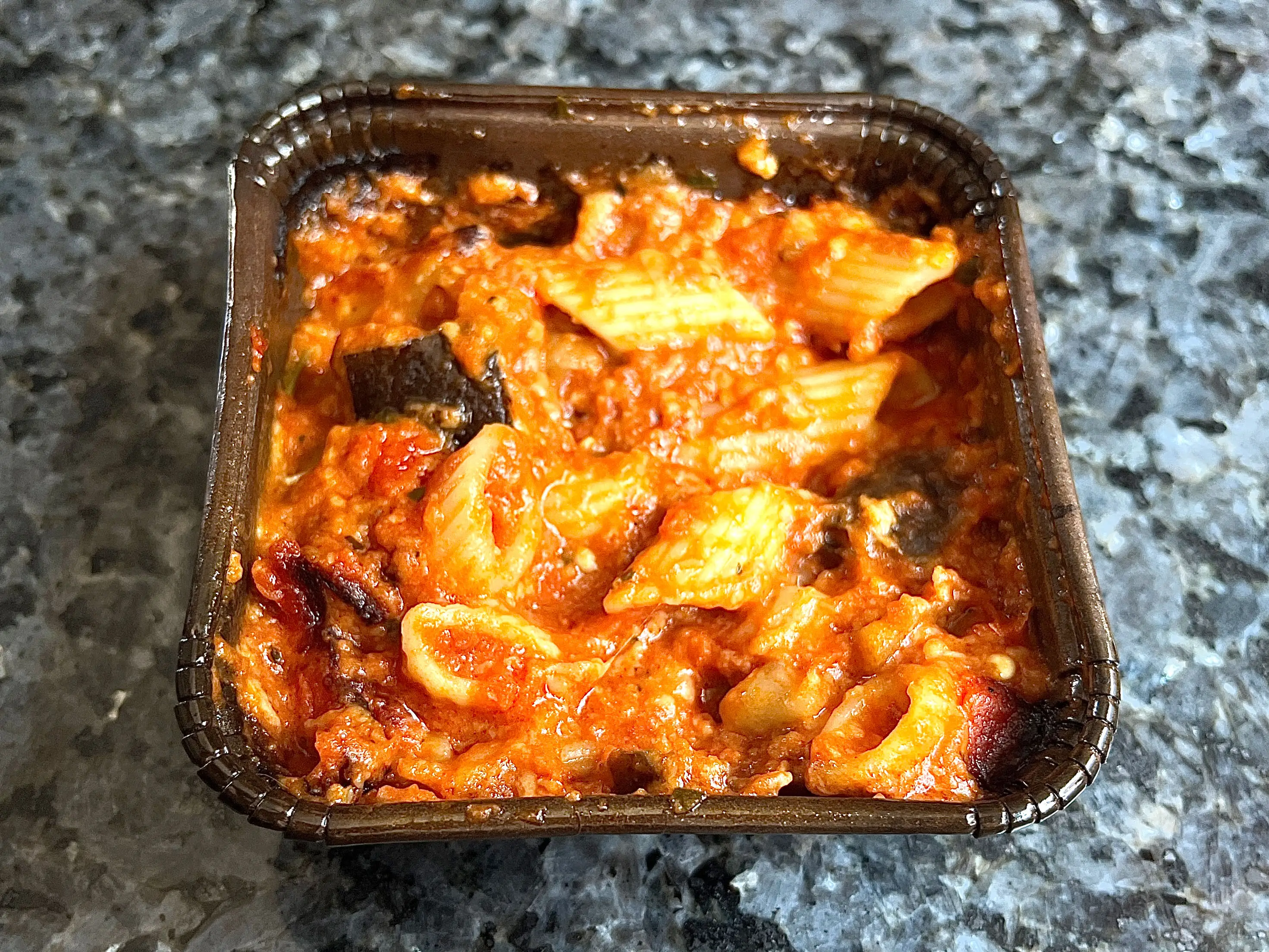 A container of pasta with red sauce and eggplant.