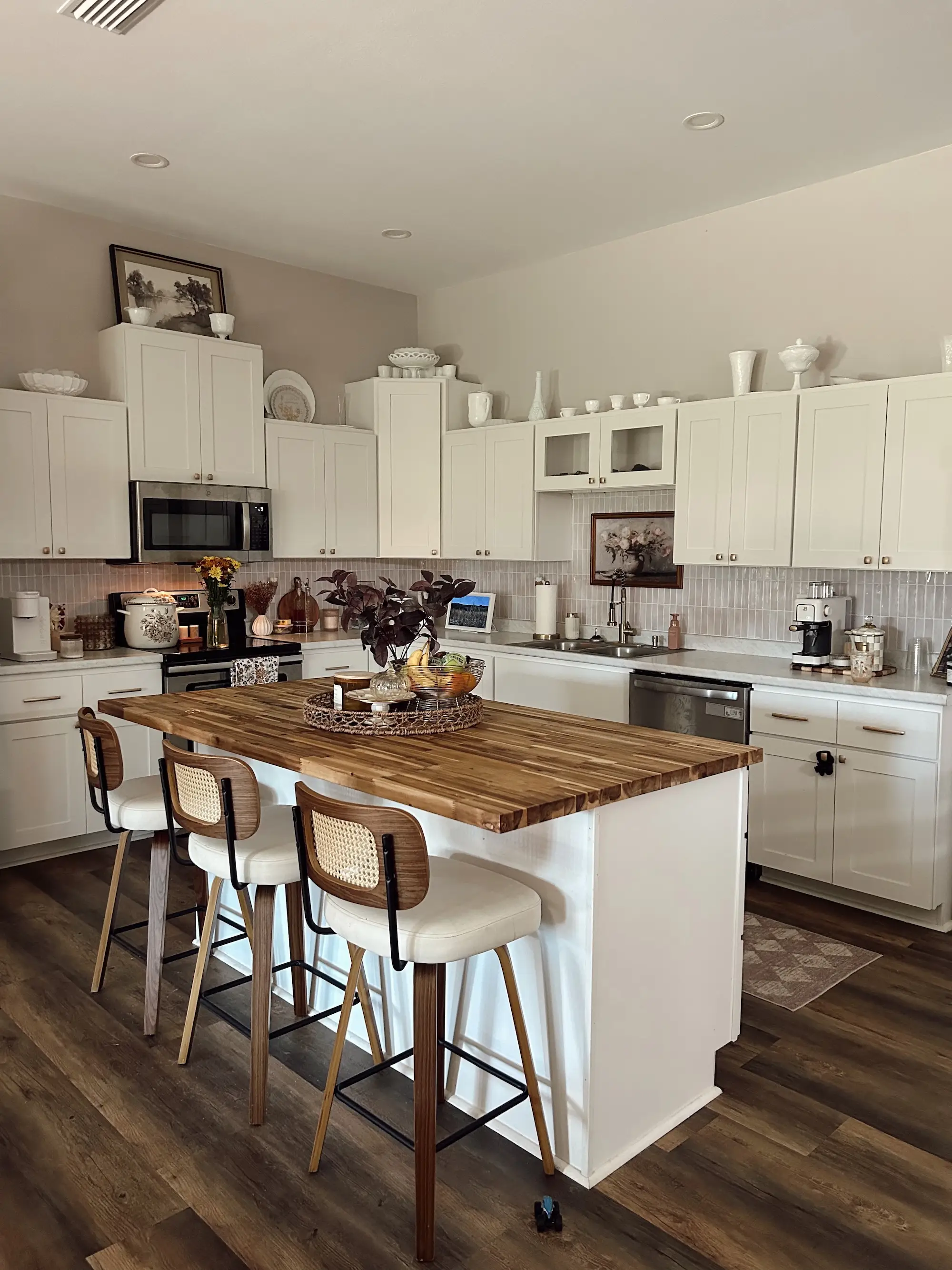 A kitchen with white countertops and cabinets. An island with a butcher block top sits in the center of the room.