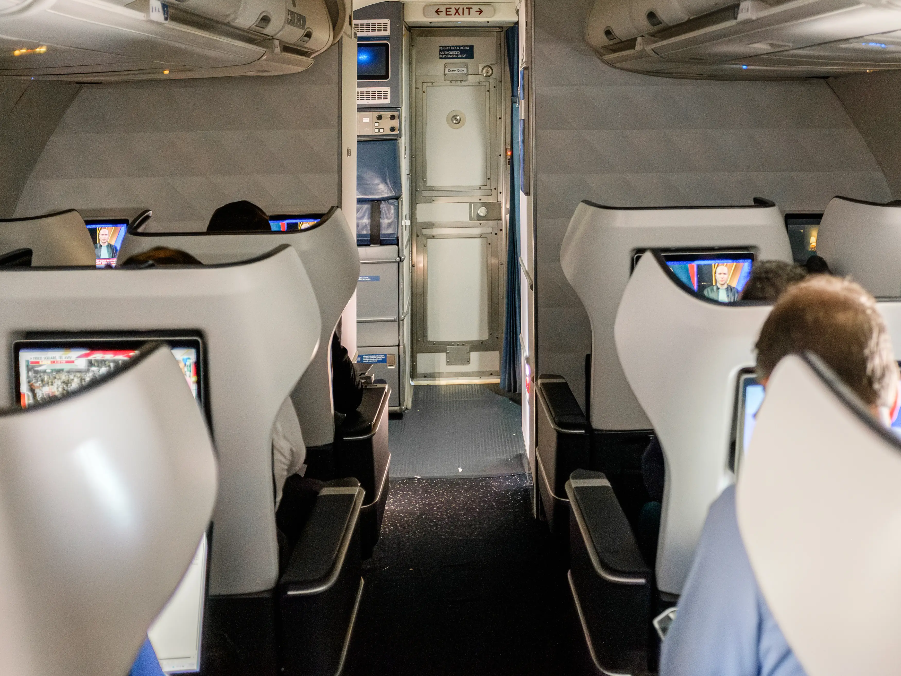 Inside a first-class flight cabin, passengers sit in winged seats on either side of the aisle.