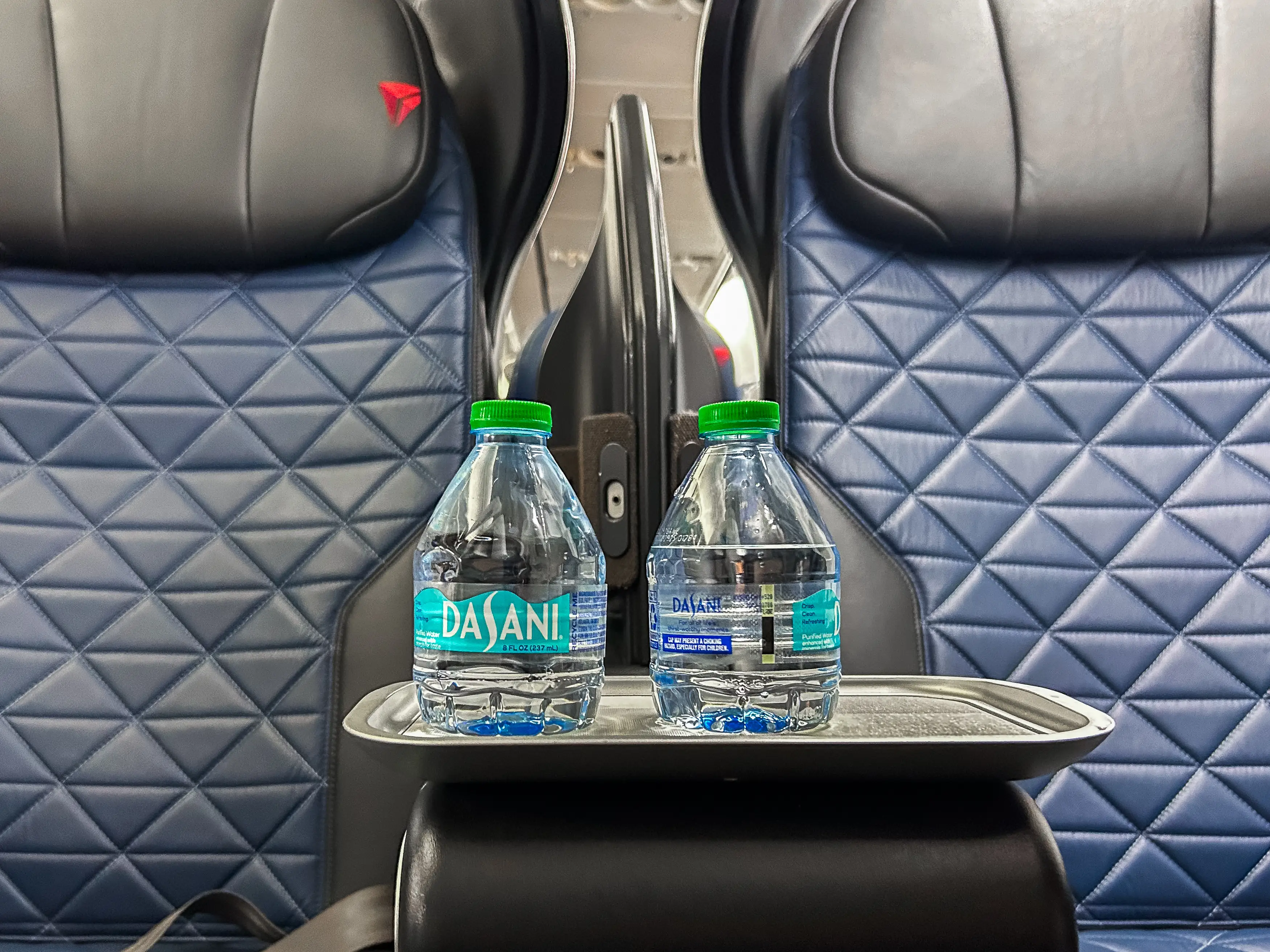 Two mini disposable water bottles on a small tray between first-class seats on a Delta flight