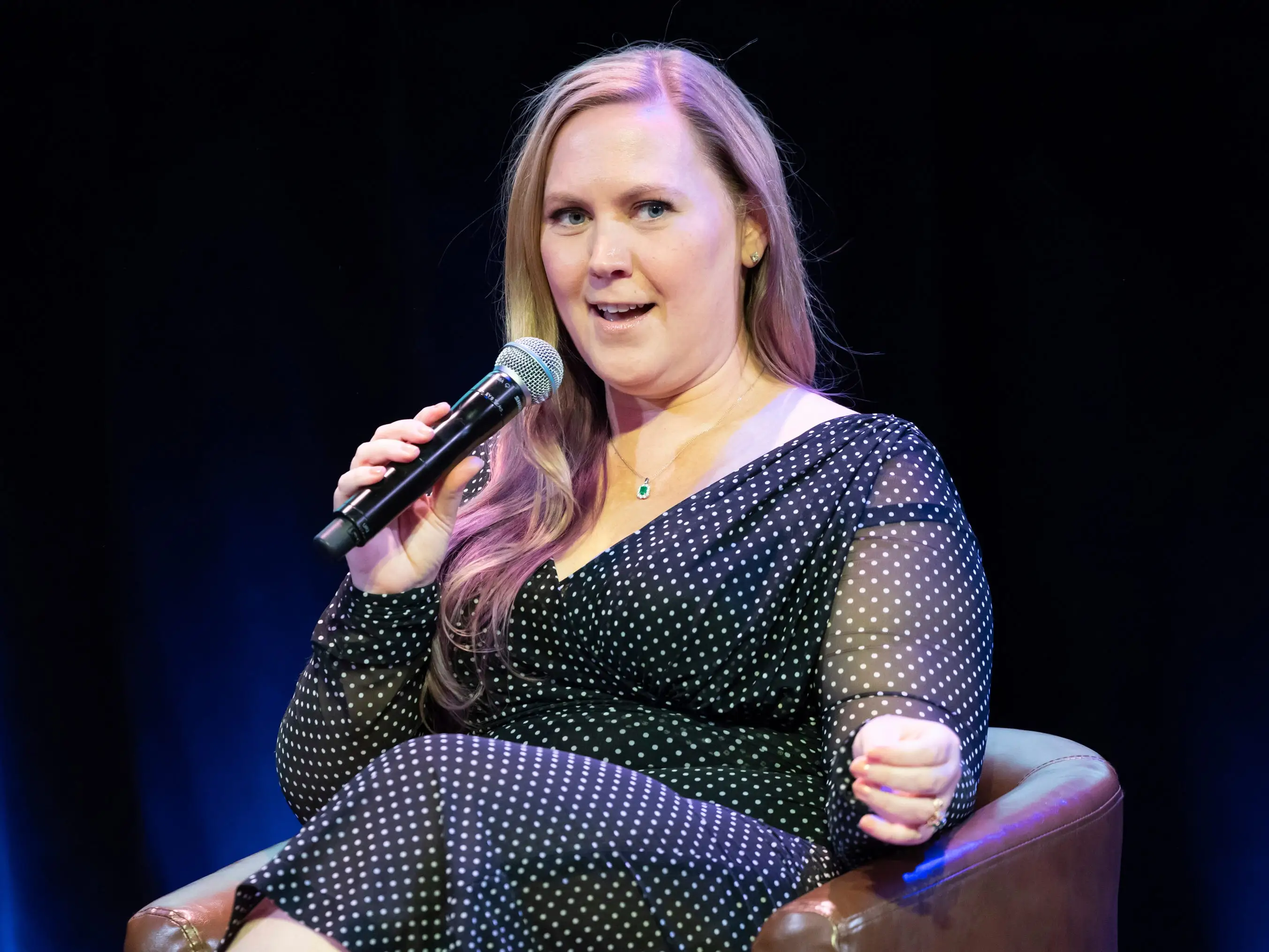 Rebecca Yarros holds a microphone and sits in a chair.