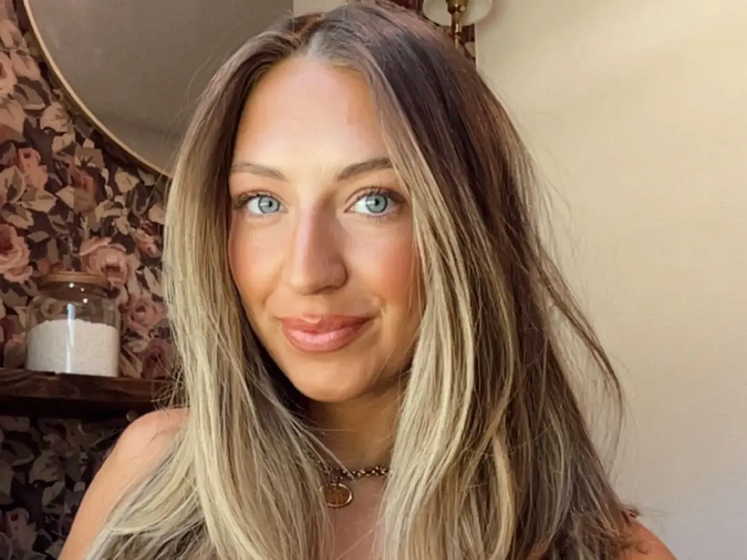 A selfie of a woman in front of a floral backdrop.