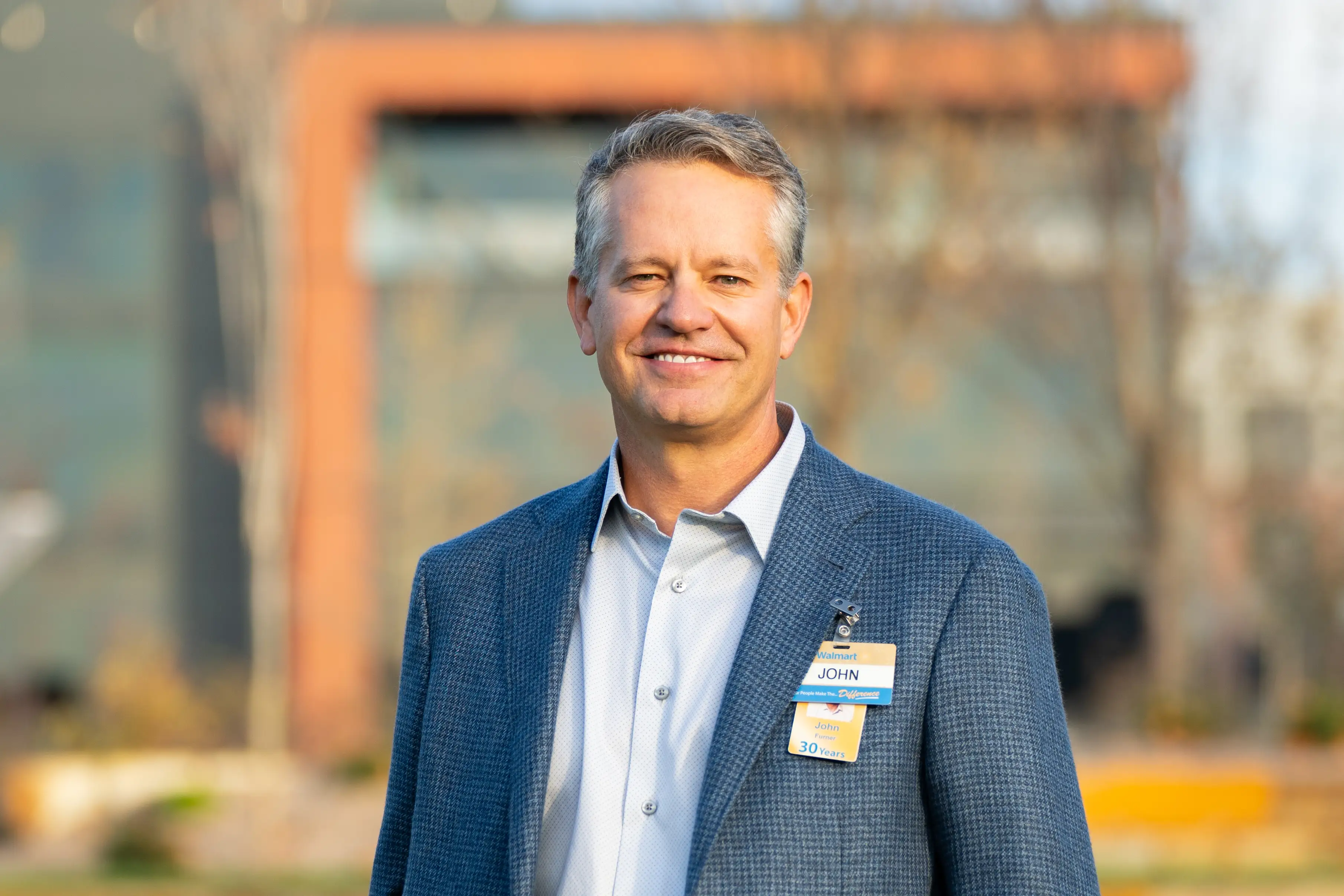 Walmart's John Furner smiles in a blue suit and a name tag.