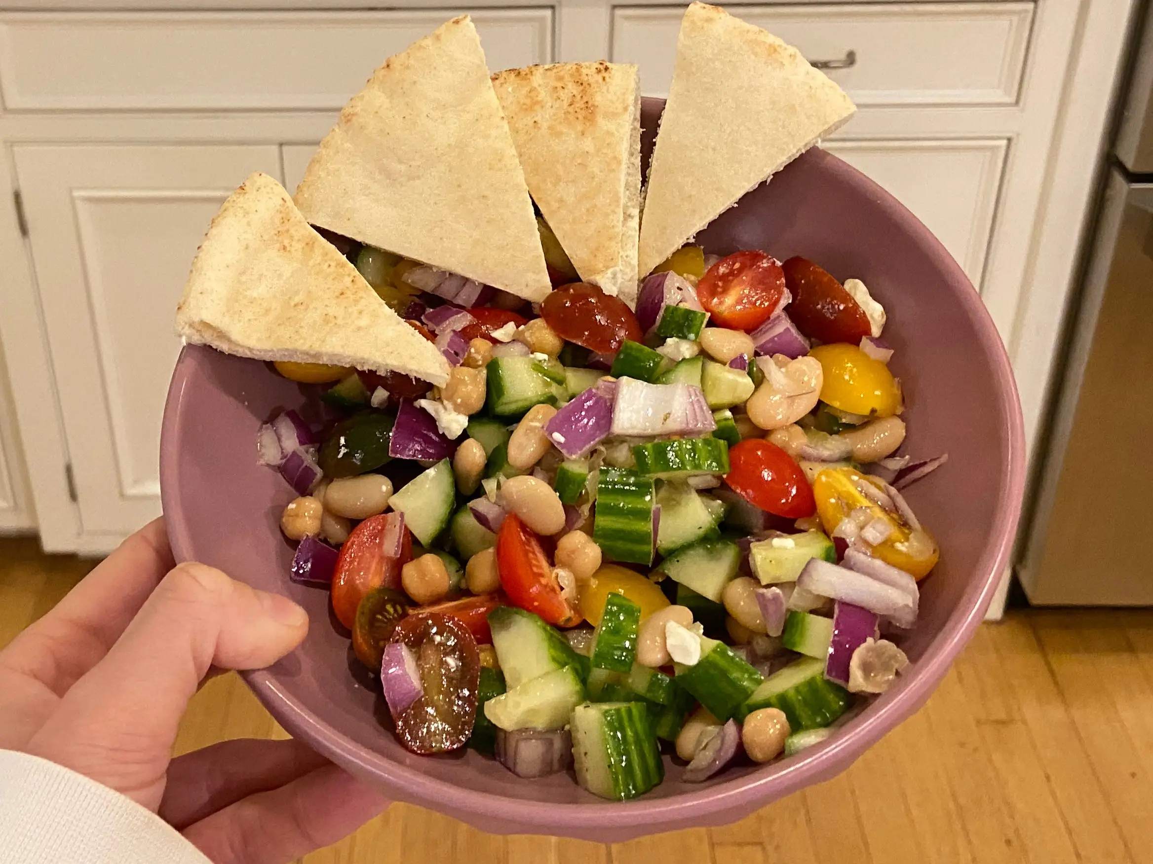 author holding bowl filled with bean salad and pita slices in kitchen