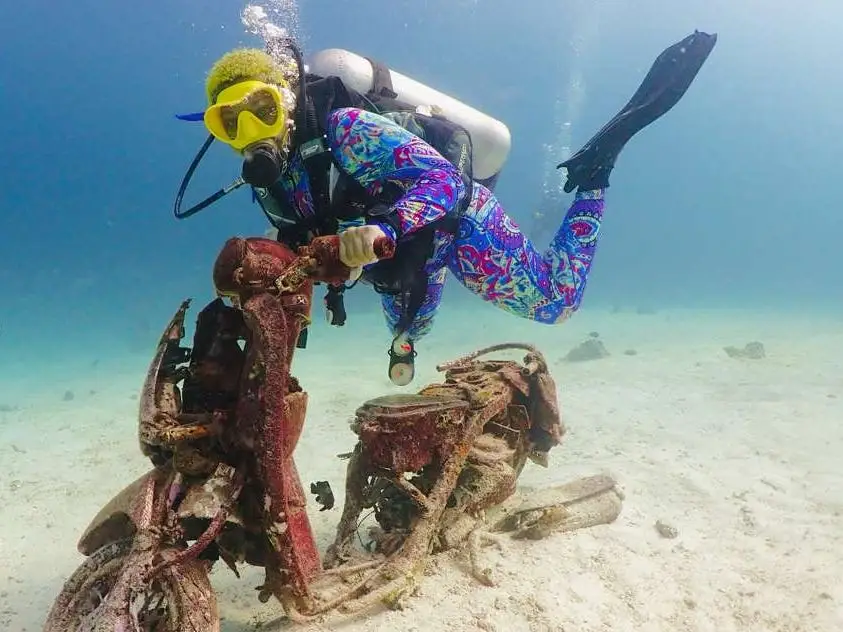 Woman with yellow hair scuba diving off Racha Yai island near a shipwreck and old motorbike.