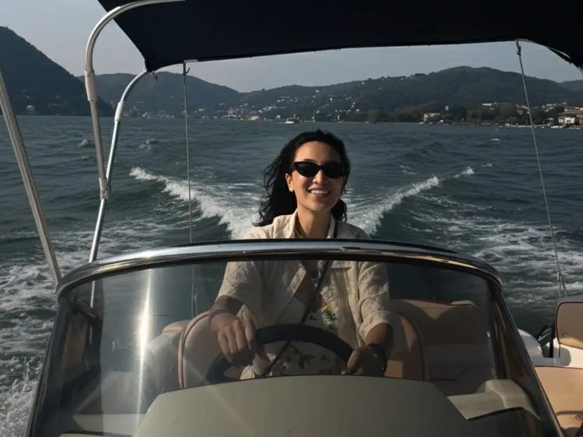 A woman wearing sunglasses is driving a boat in Lake Como, Italy.