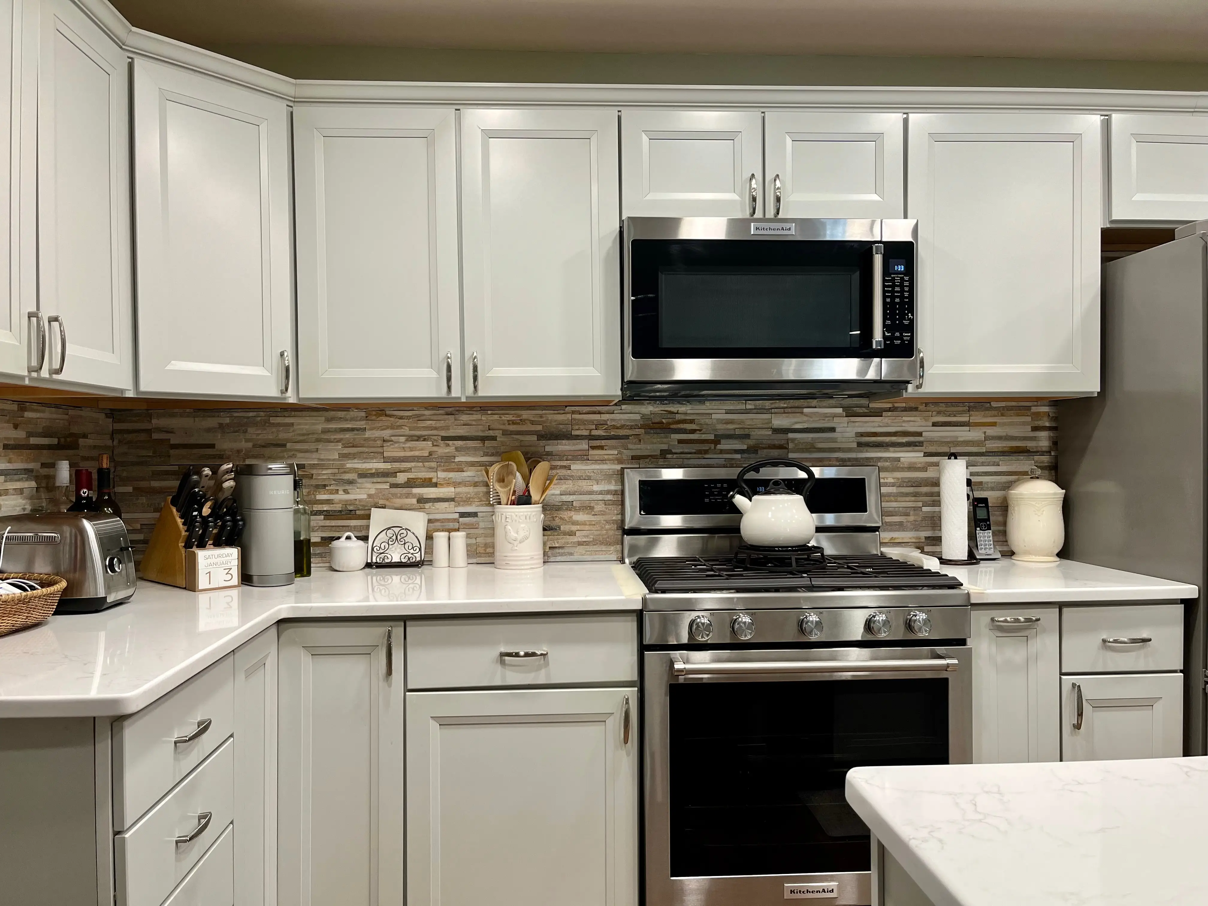 Microwave over stove in kitchen with stone backsplash, white cabinets