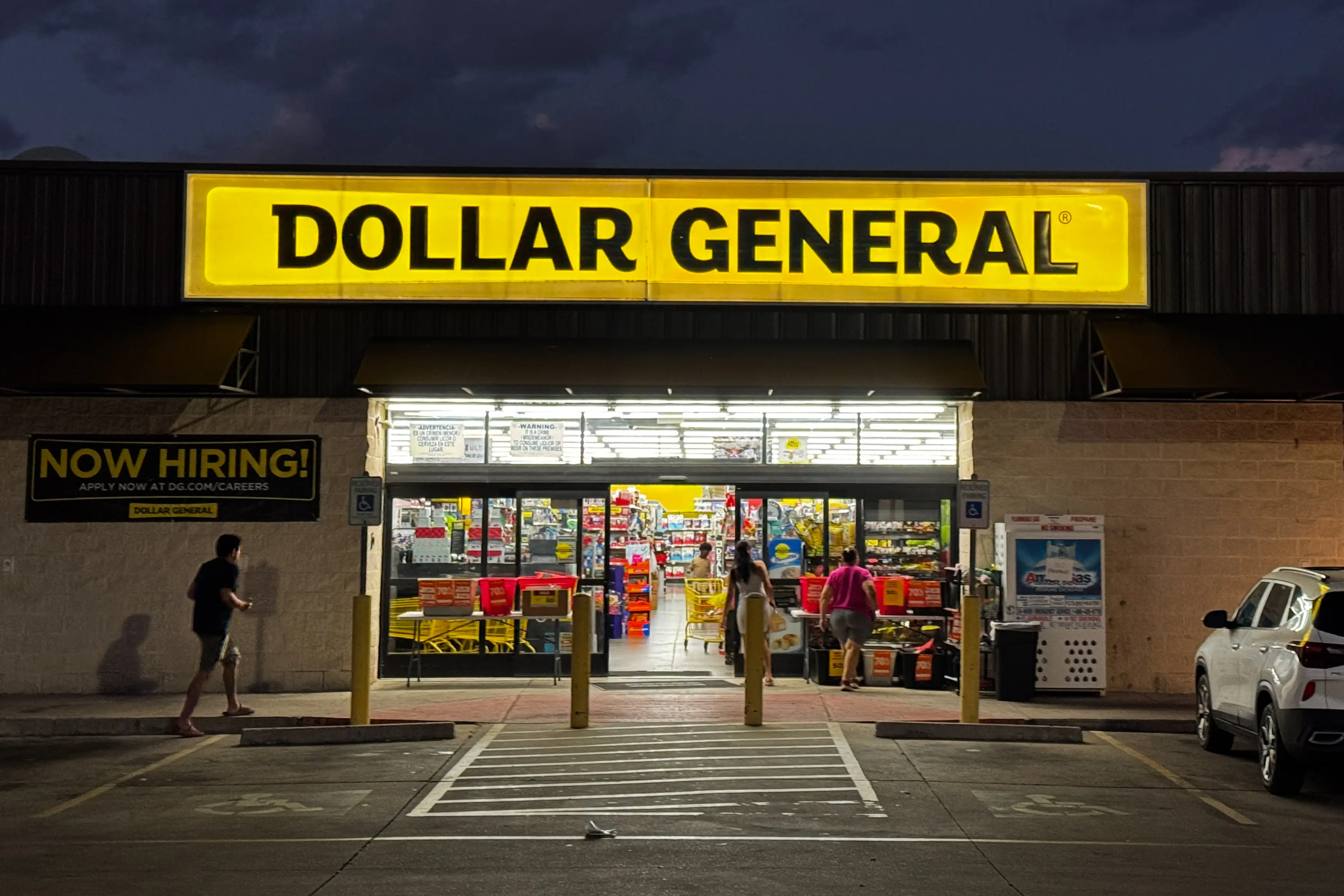 A Dollar General store is seen at night as customers walk in the main entrance from the parking lot.