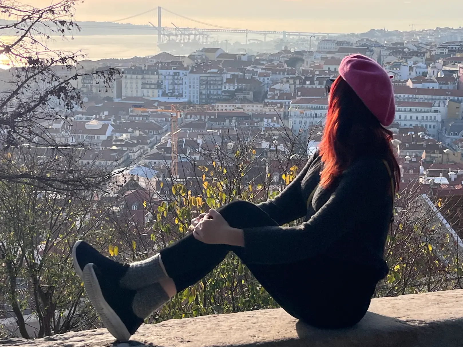 The writer posing on a ledge in Portugal, overlooking houses.