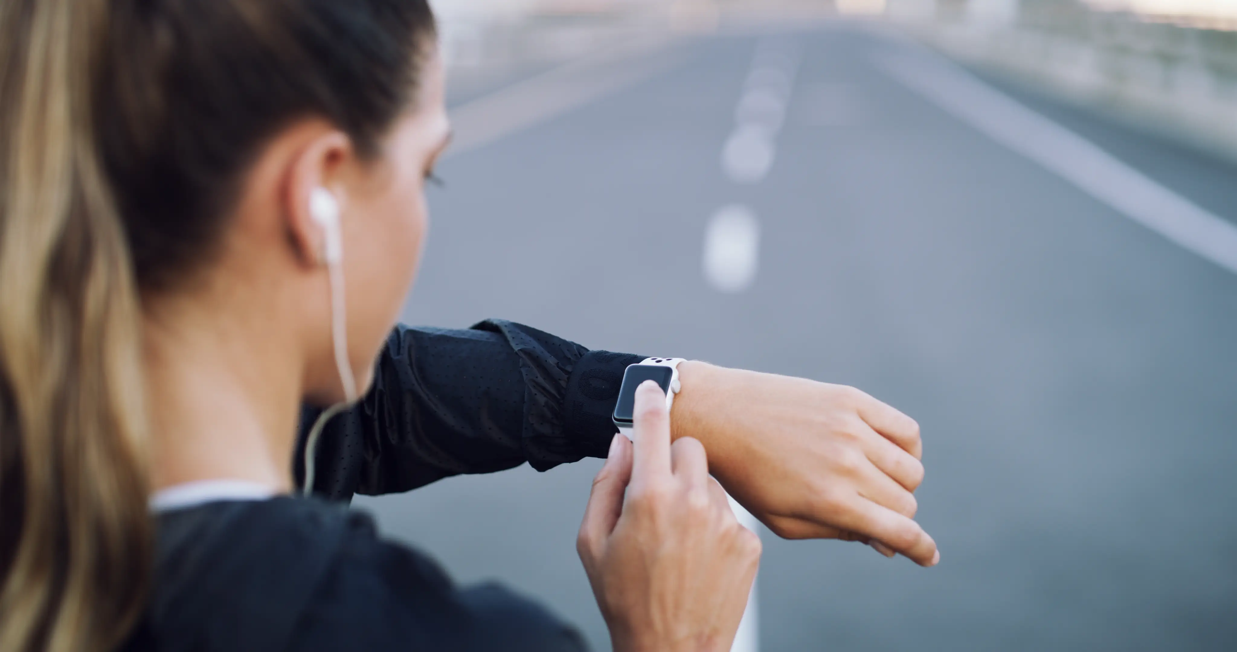 A woman pictured in an out-of-focus side view checking her smartwatch on a run