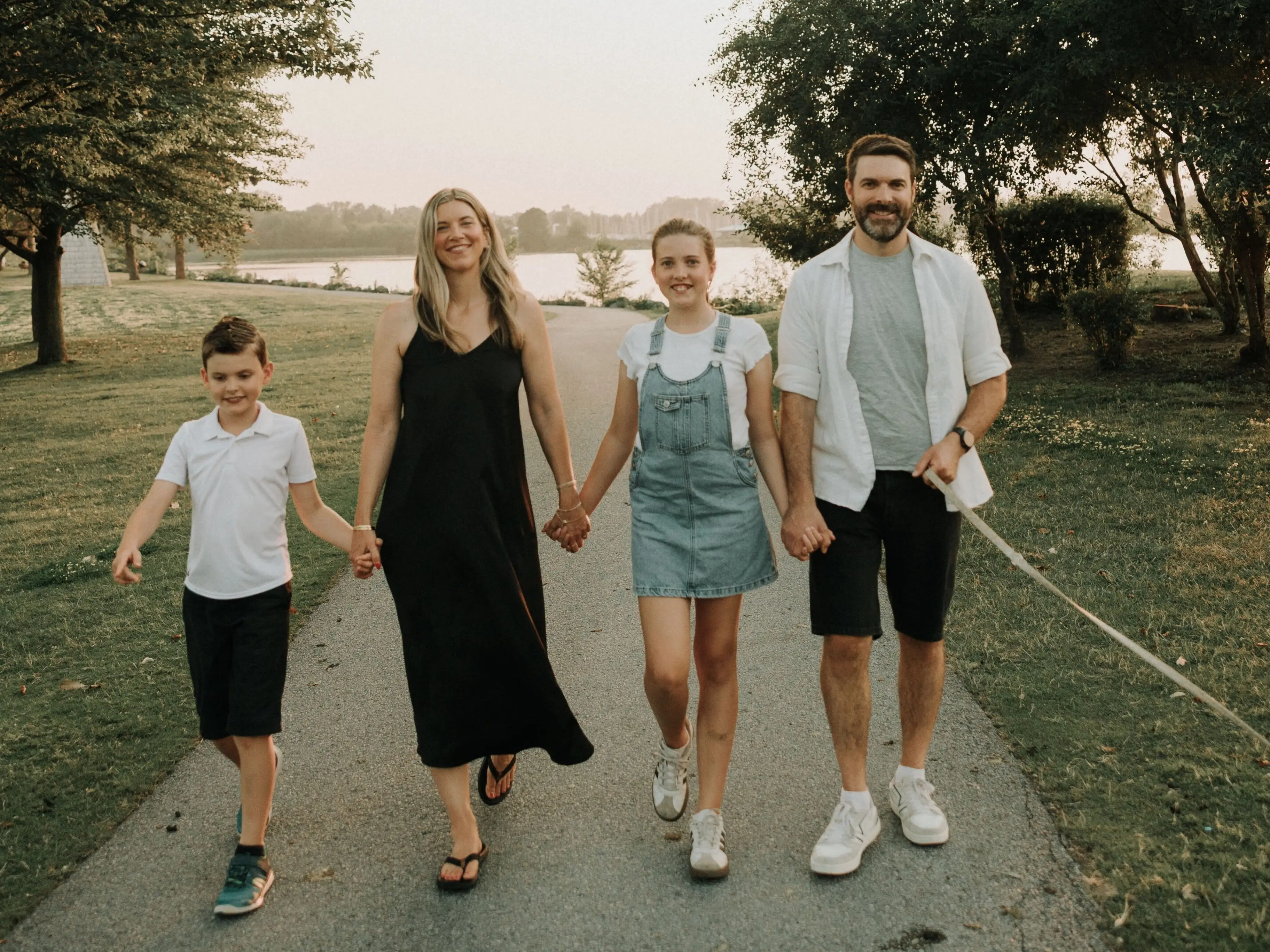 Family of four walking and holding hands with trees in the background.