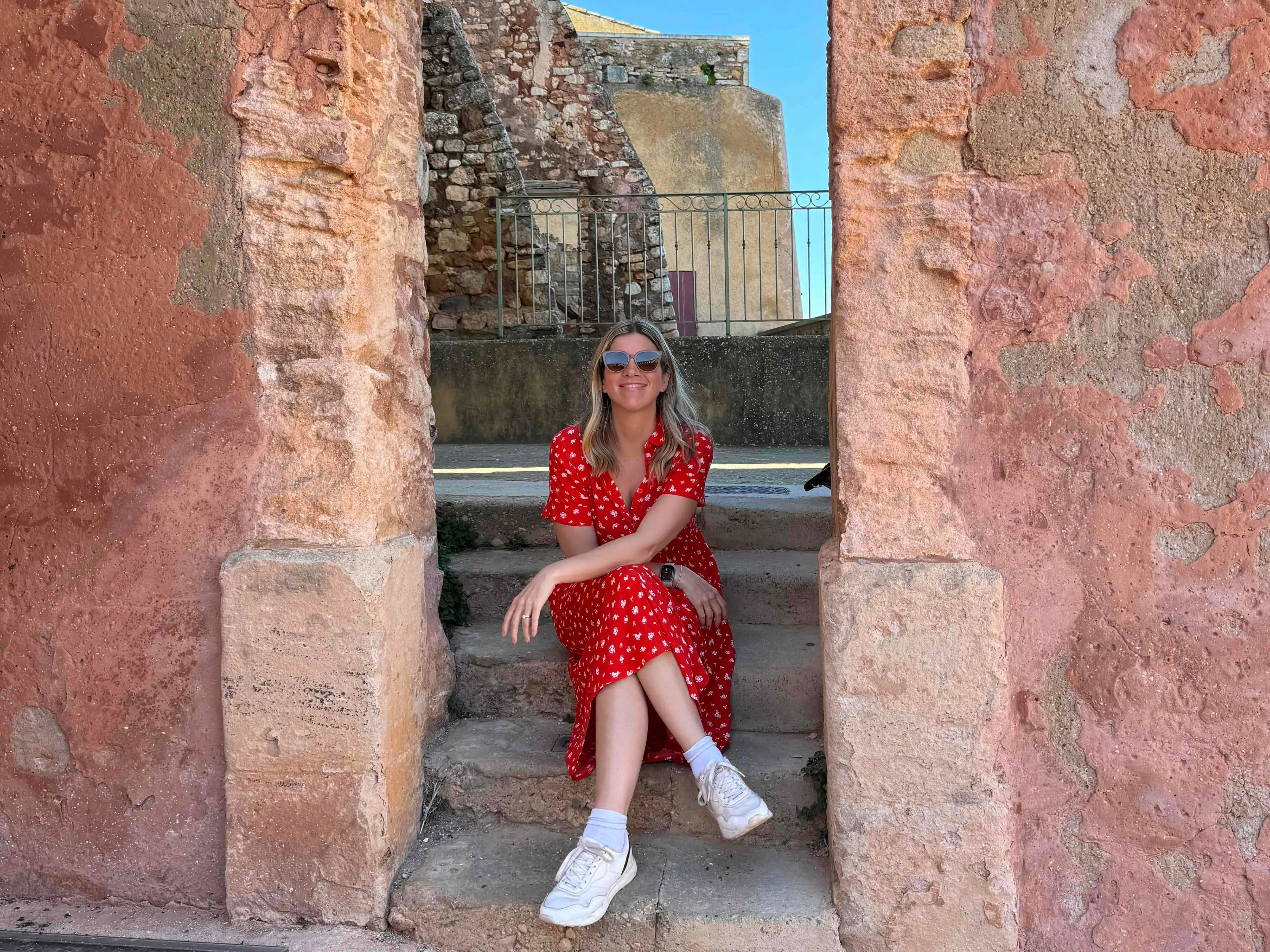 Woman in a red dress seated under a stone arch in France.