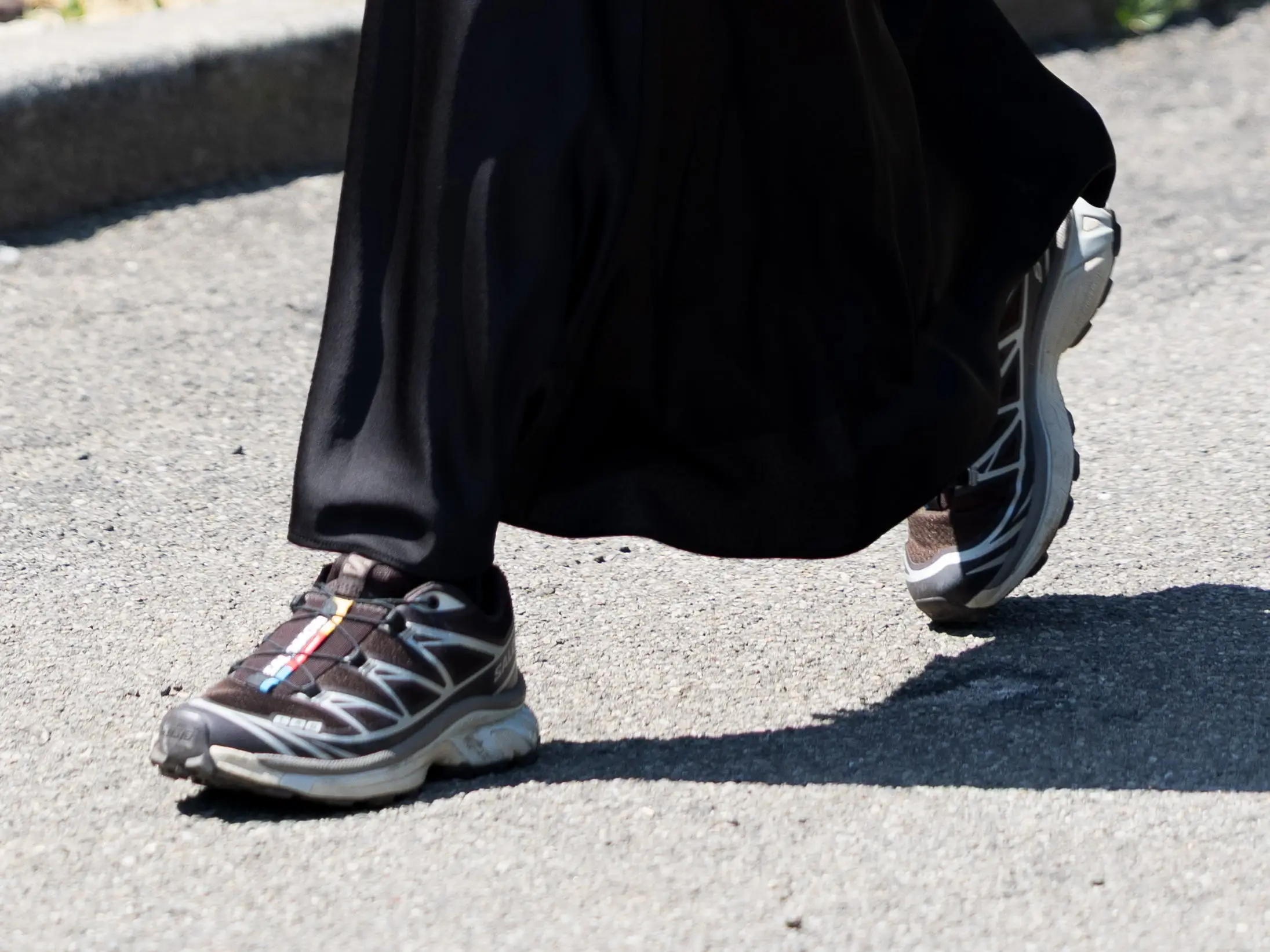 A close-up of Salomon athletic sneakers paired with a long black satin skirt.